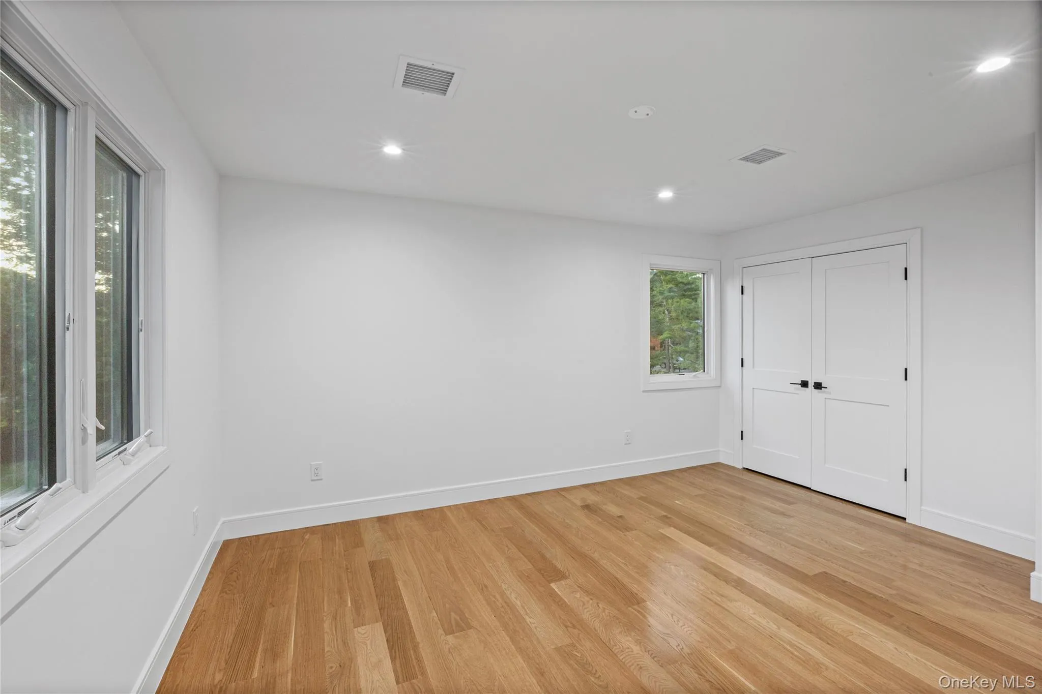 Spacious room featuring wood-finish flooring, recessed lighting, and multiple windows Spacious room featuring wood-finish flooring, recessed lighting, and multiple windows