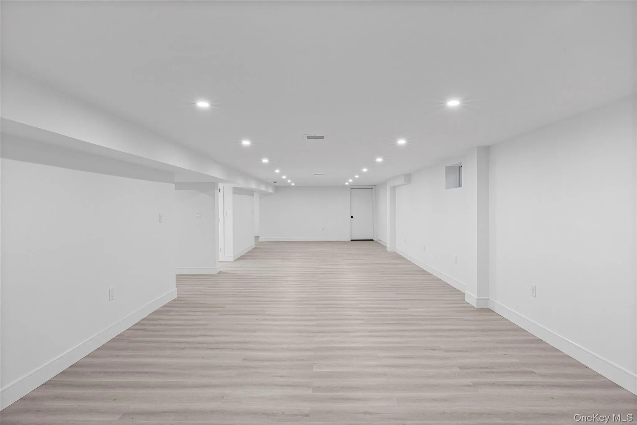 Spacious lower level featuring light wood-finish flooring, recessed lighting, and a white baluster staircase with wood handrails Spacious lower level featuring light wood-finish flooring, recessed lighting, and a white baluster staircase with wood handrails