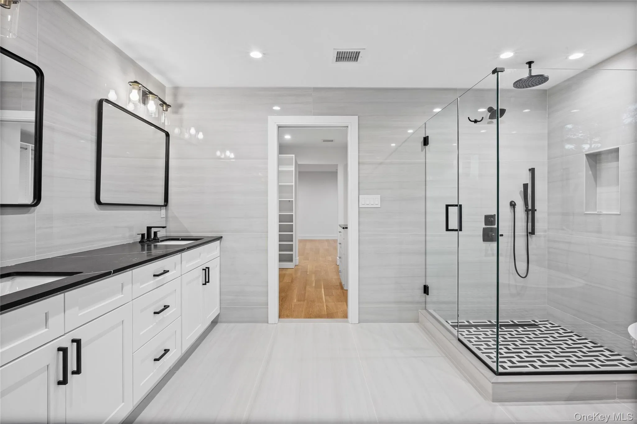 Contemporary bathroom featuring a spacious glass-enclosed shower with black and white patterned tile flooring, a rainfall showerhead, and a wall-mounted shower system Contemporary bathroom featuring a spacious glass-enclosed shower with black and white patterned tile flooring, a rainfall showerhead, and a wall-mounted shower system