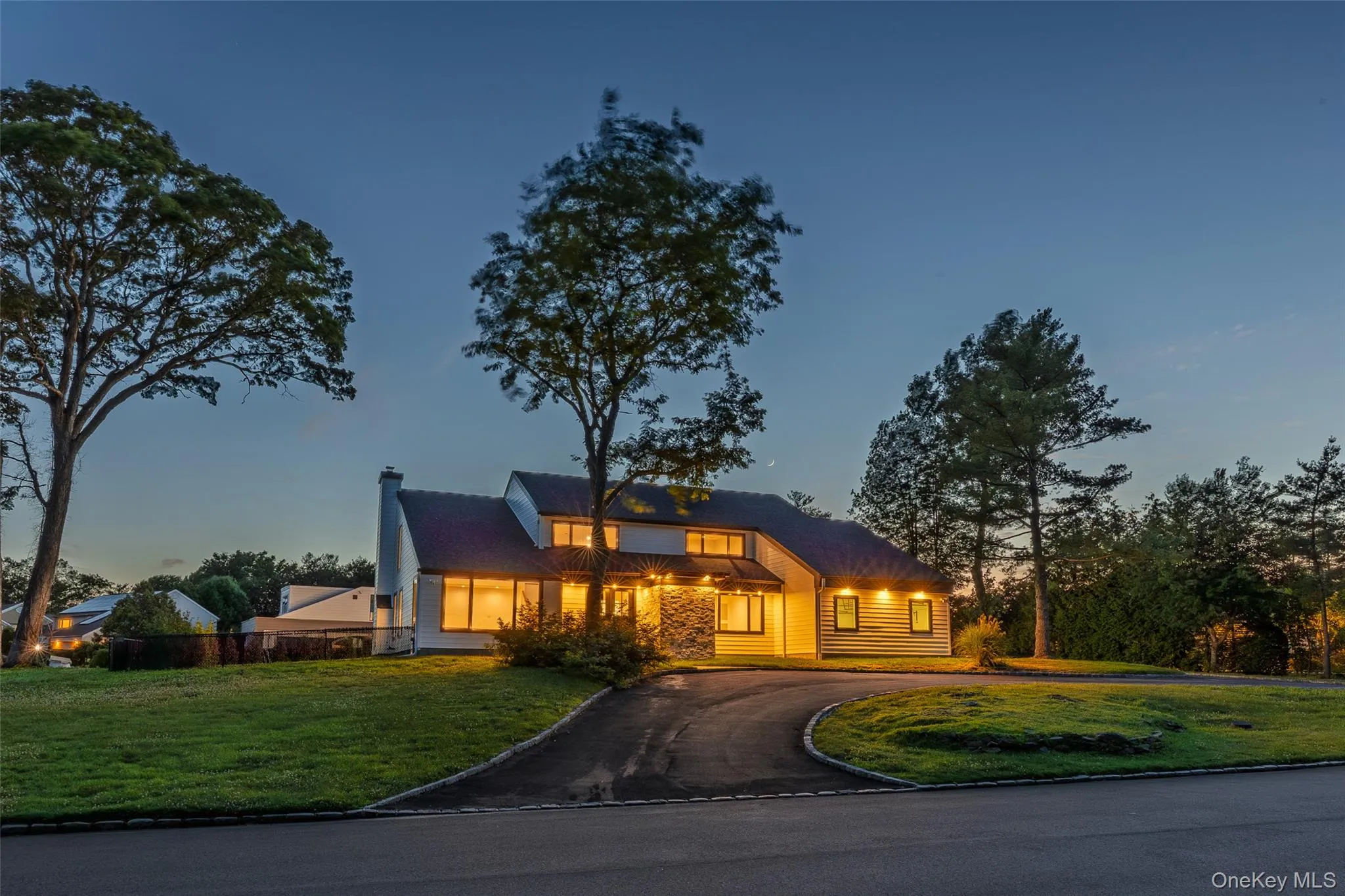 Contemporary residence featuring a paved circular driveway, stone accents, multiple windows, and a shingled roof Contemporary residence featuring a paved circular driveway, stone accents, multiple windows, and a shingled roof
