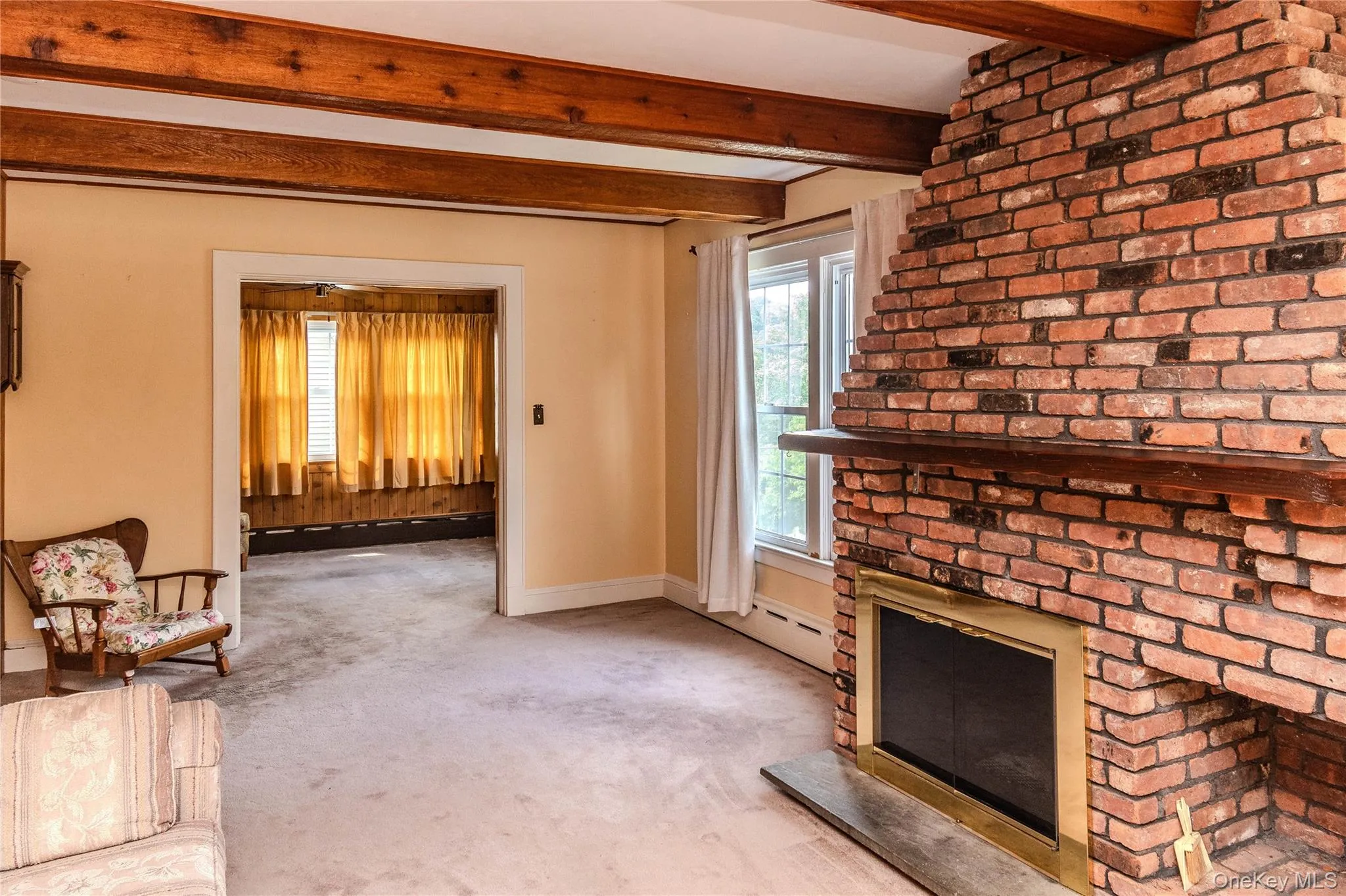Exposed wood ceiling beams accentuating a brick fireplace with a wood mantle and brass-framed insert Exposed wood ceiling beams accentuating a brick fireplace with a wood mantle and brass-framed insert