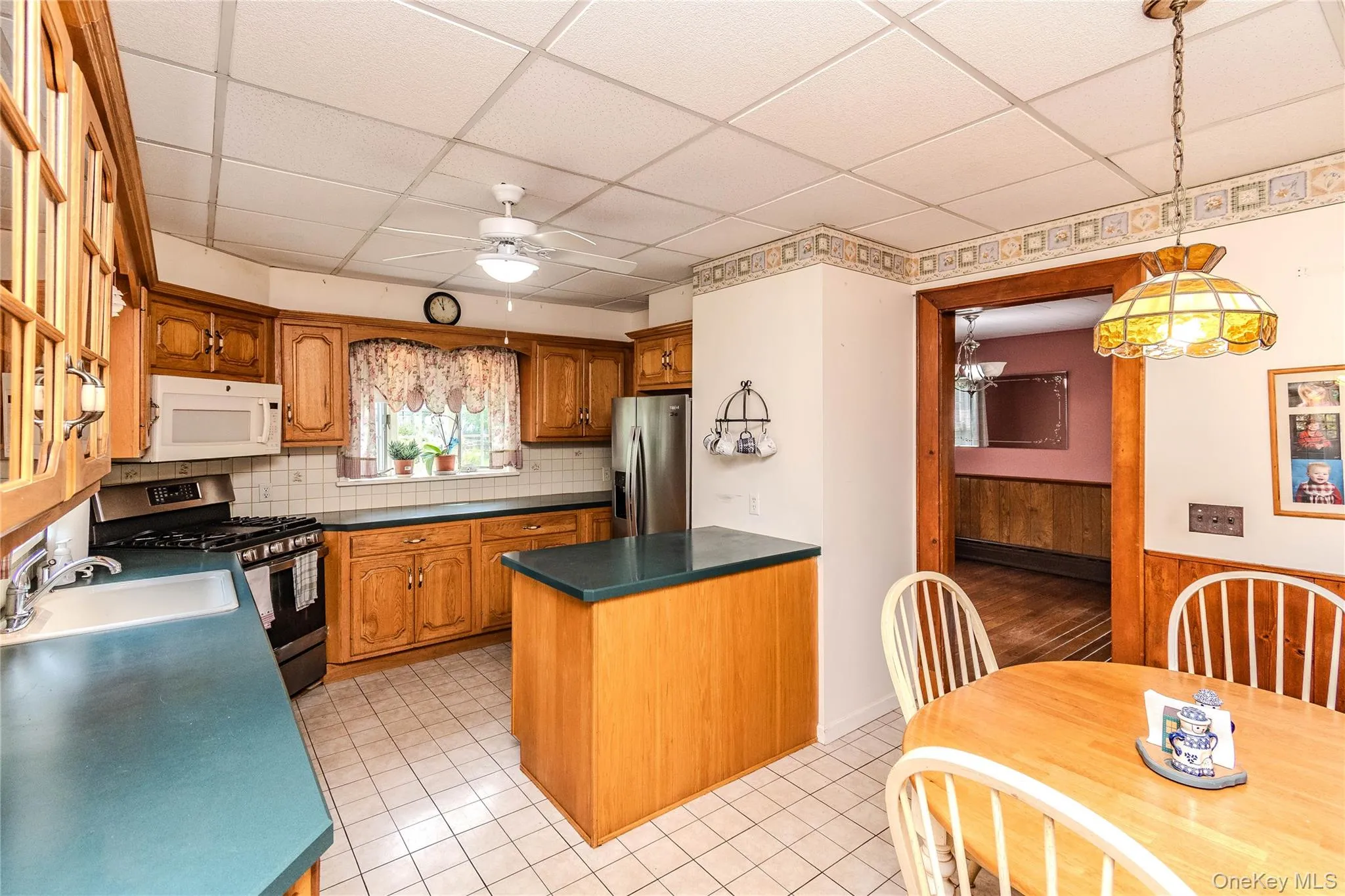 Kitchen featuring wood cabinetry, a stainless steel refrigerator, white tile backsplash, an overhead microwave, and a gas range Kitchen featuring wood cabinetry, a stainless steel refrigerator, white tile backsplash, an overhead microwave, and a gas range