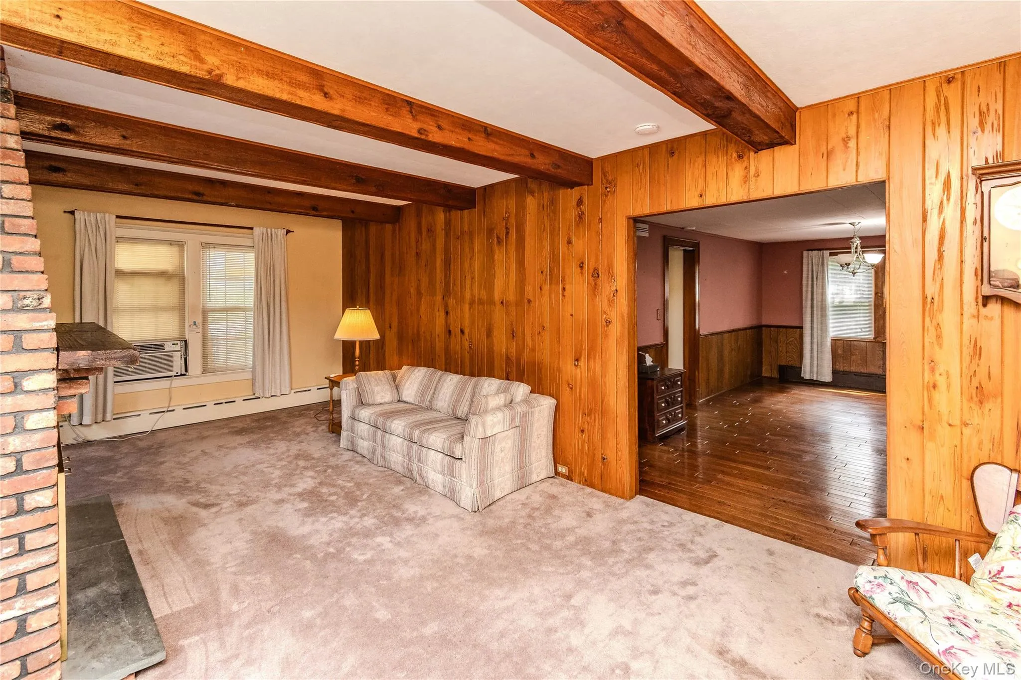 Living space featuring wood paneling, exposed wood ceiling beams, a brick fireplace surround with a stone hearth, and carpeted flooring Living space featuring wood paneling, exposed wood ceiling beams, a brick fireplace surround with a stone hearth, and carpeted flooring