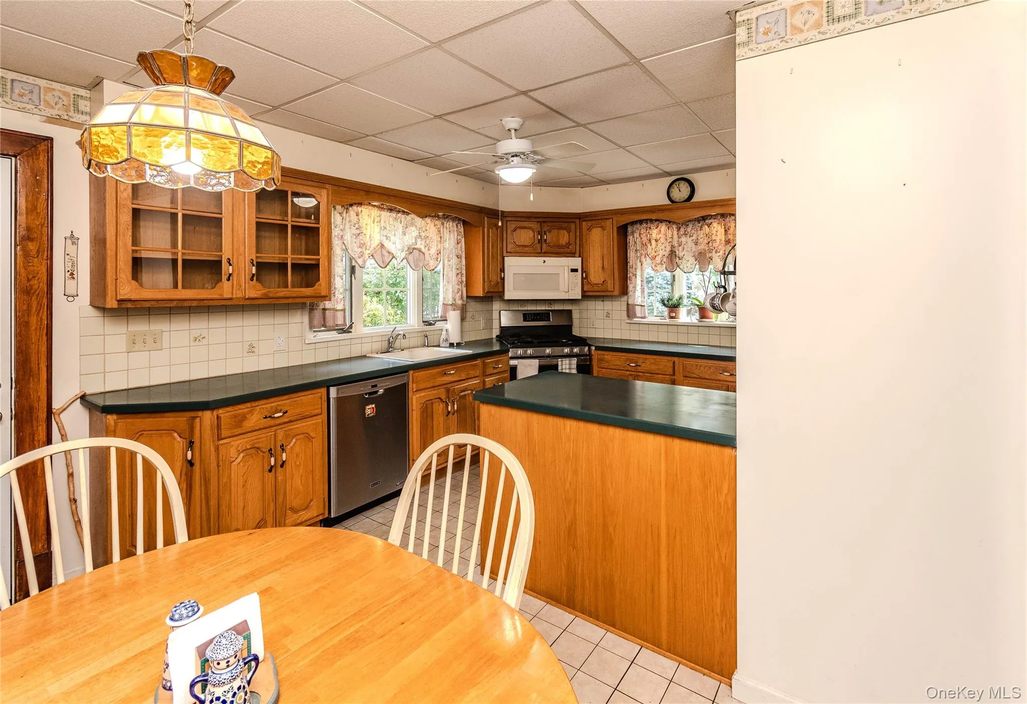 Kitchen featuring wood cabinetry, a center island with countertop, stainless steel dishwasher, and white tile flooring Kitchen featuring wood cabinetry, a center island with countertop, stainless steel dishwasher, and white tile flooring