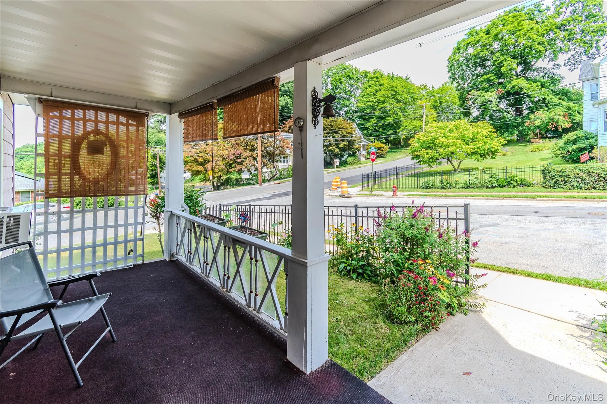 Covered front porch featuring a black floor covering, white lattice railing, and decorative bamboo shades Covered front porch featuring a black floor covering, white lattice railing, and decorative bamboo shades