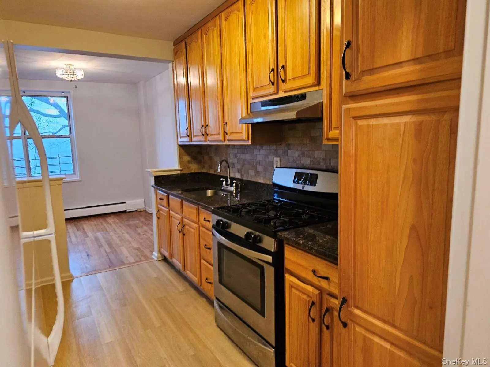 Kitchen with stainless steel gas range, dark stone counters, light wood-style floors, under cabinet range hood, and baseboard heating Kitchen with stainless steel gas range, dark stone counters, light wood-style floors, under cabinet range hood, and baseboard heating