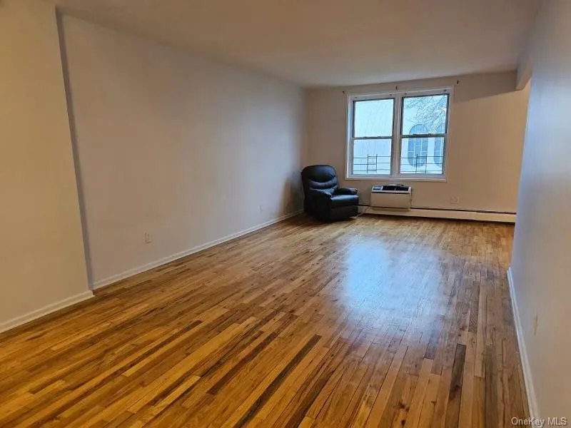 Spare room with light wood-style flooring, an AC wall unit, and a baseboard radiator Spare room with light wood-style flooring, an AC wall unit, and a baseboard radiator