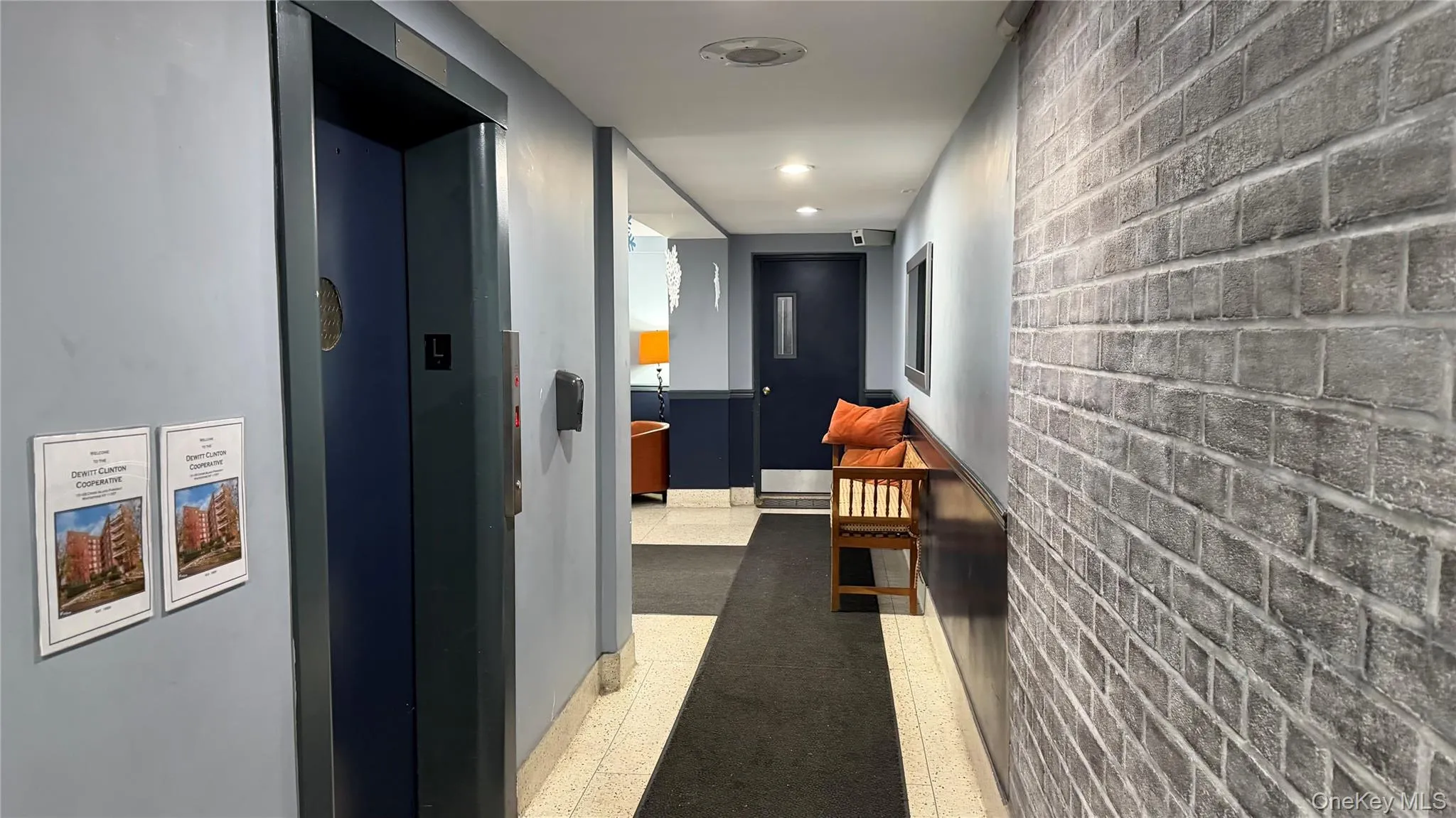 Hall with elevator, dark speckled floor, brick wall, and recessed lighting Hall with elevator, dark speckled floor, brick wall, and recessed lighting