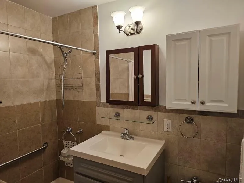Bathroom featuring tiled shower, vanity, and tile walls Bathroom featuring tiled shower, vanity, and tile walls