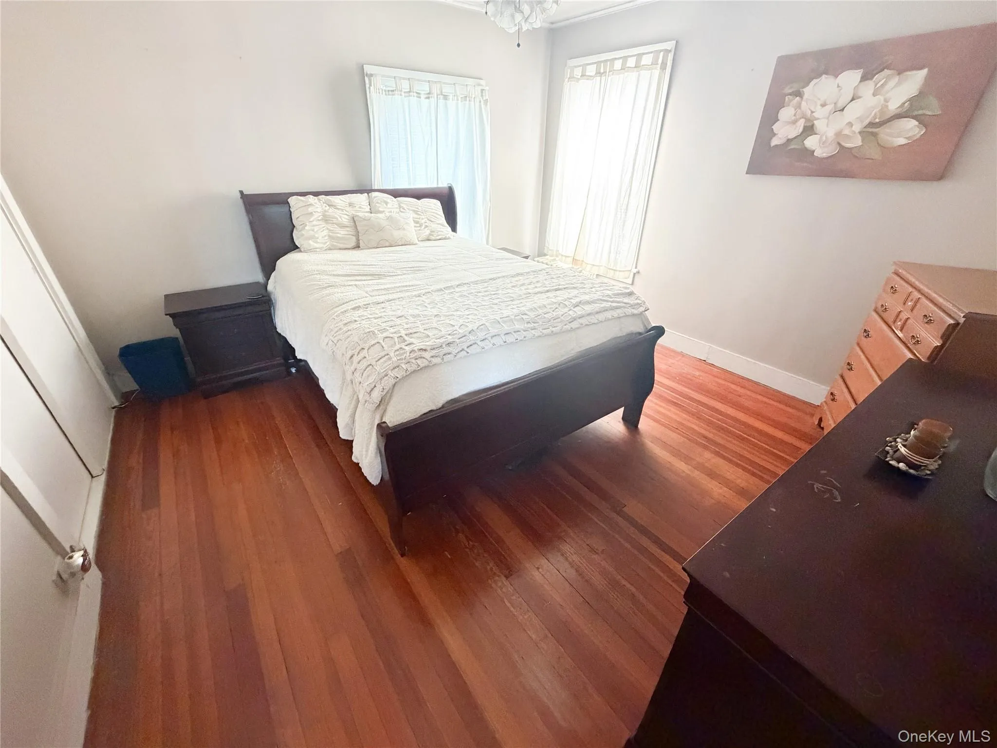 Room featuring wood-finish flooring, light-toned wall paint, and a window with vertical blinds Room featuring wood-finish flooring, light-toned wall paint, and a window with vertical blinds