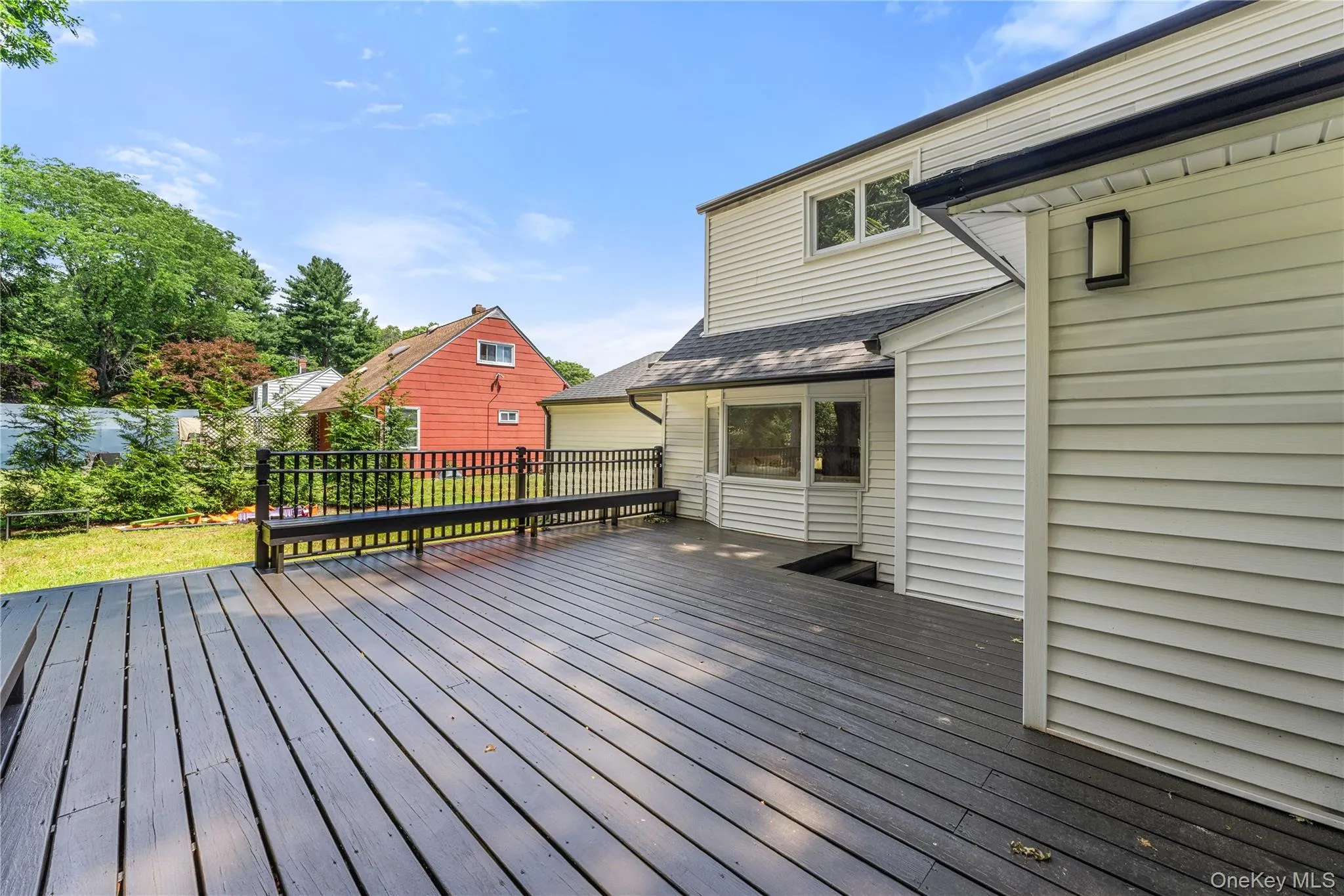 Spacious dark-toned deck featuring a built-in bench, black railing, and multiple steps for backyard access Spacious dark-toned deck featuring a built-in bench, black railing, and multiple steps for backyard access