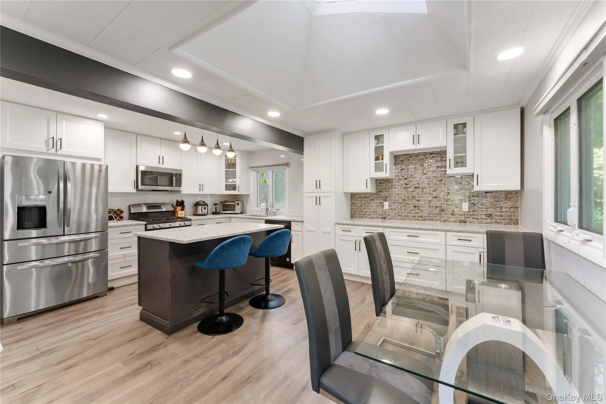 Gourmet kitchen featuring stainless steel appliances, white cabinetry, a central island with countertop seating, wood-finish flooring, and a skylight Gourmet kitchen featuring stainless steel appliances, white cabinetry, a central island with countertop seating, wood-finish flooring, and a skylight