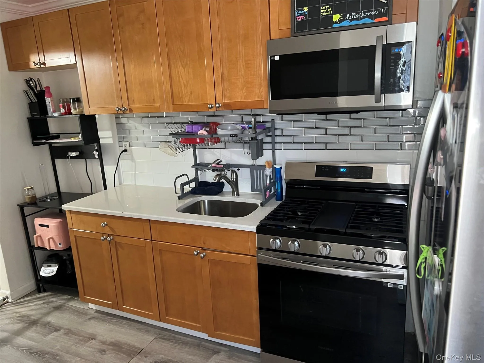 Kitchen featuring wood cabinetry, stainless steel appliances, a subway tile backsplash, white countertops, and wood-finish flooring Kitchen featuring wood cabinetry, stainless steel appliances, a subway tile backsplash, white countertops, and wood-finish flooring