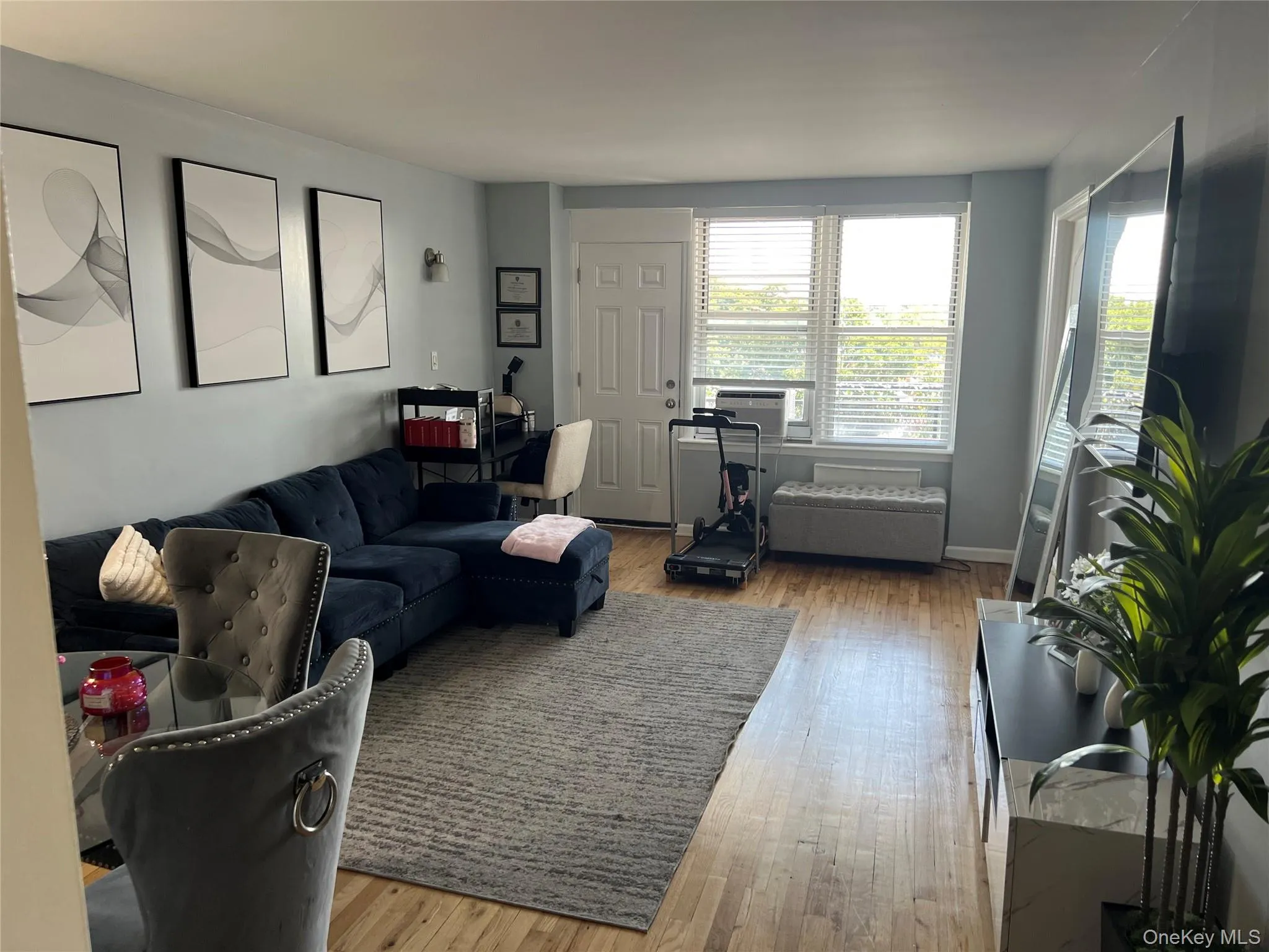 Living area featuring wood-finish flooring, light blue wall paint, and a window with blinds Living area featuring wood-finish flooring, light blue wall paint, and a window with blinds