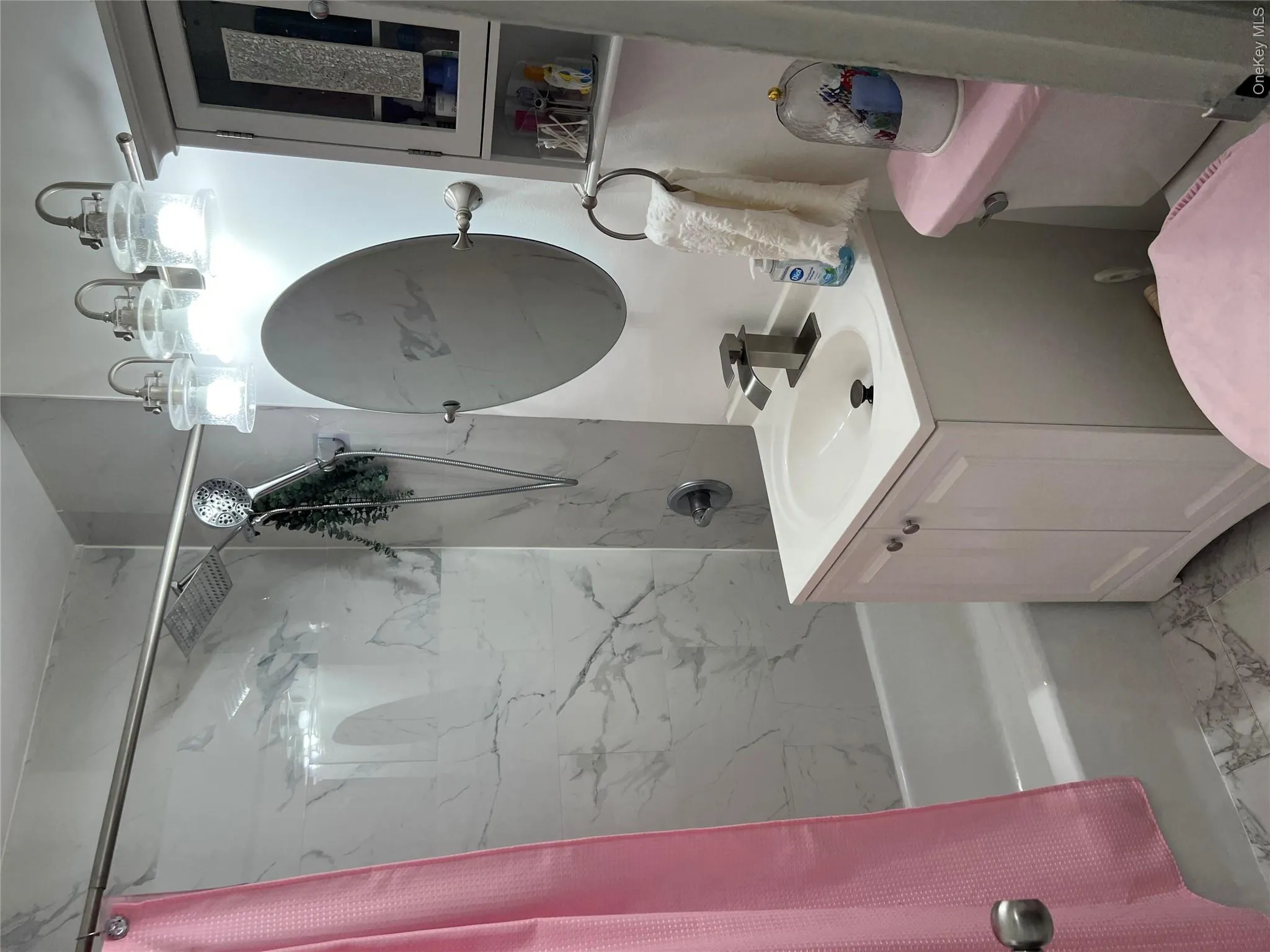 Full bathroom featuring a single vanity with a white basin and cabinet storage, a circular mirror, and a three-light vanity fixture Full bathroom featuring a single vanity with a white basin and cabinet storage, a circular mirror, and a three-light vanity fixture