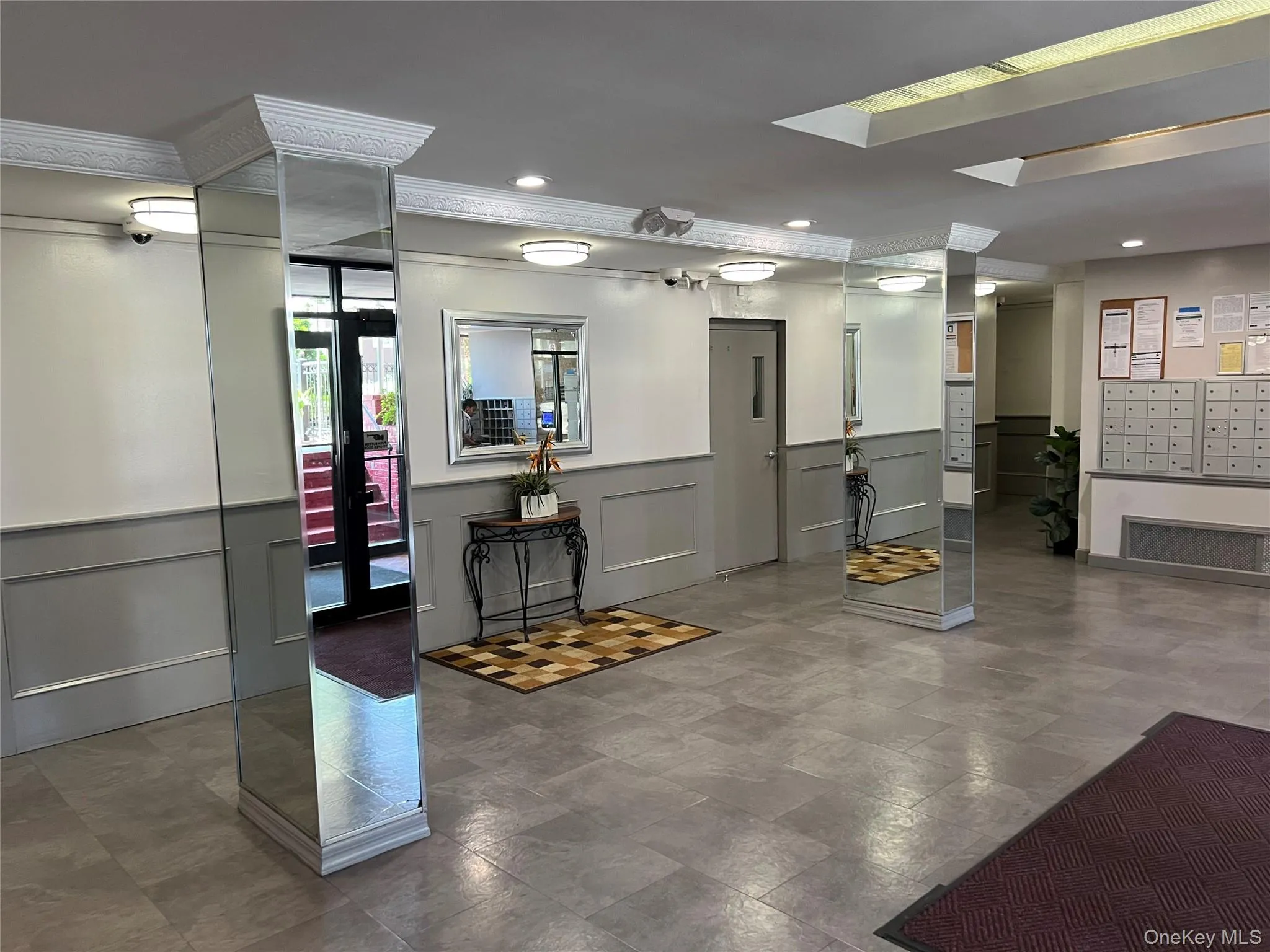 Building lobby featuring grey tile flooring, wainscoting details, mirrored columns, and multiple wall-mounted mailboxes Building lobby featuring grey tile flooring, wainscoting details, mirrored columns, and multiple wall-mounted mailboxes