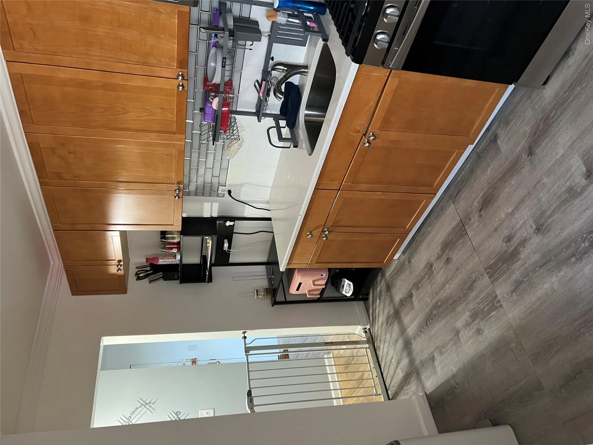 Kitchen featuring wood-finish cabinetry, white countertops, tile backsplash, stainless steel sink, and wood-finish flooring Kitchen featuring wood-finish cabinetry, white countertops, tile backsplash, stainless steel sink, and wood-finish flooring