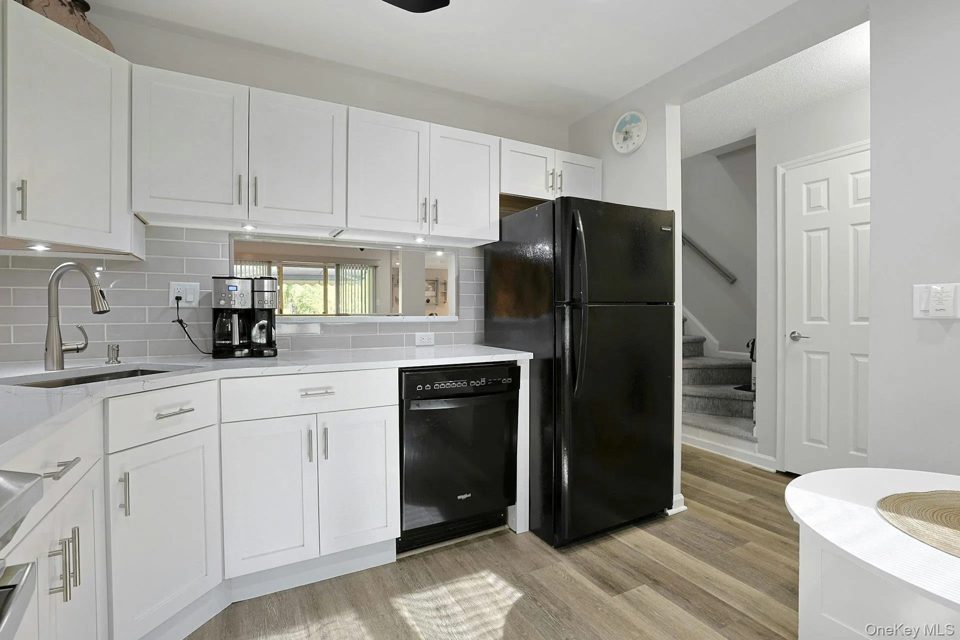 Kitchen featuring white shaker cabinetry, light gray subway tile backsplash, quartz countertops, under cabinet ligjhting and wood-finish flooring Kitchen featuring white shaker cabinetry, light gray subway tile backsplash, quartz countertops, under cabinet ligjhting and wood-finish flooring