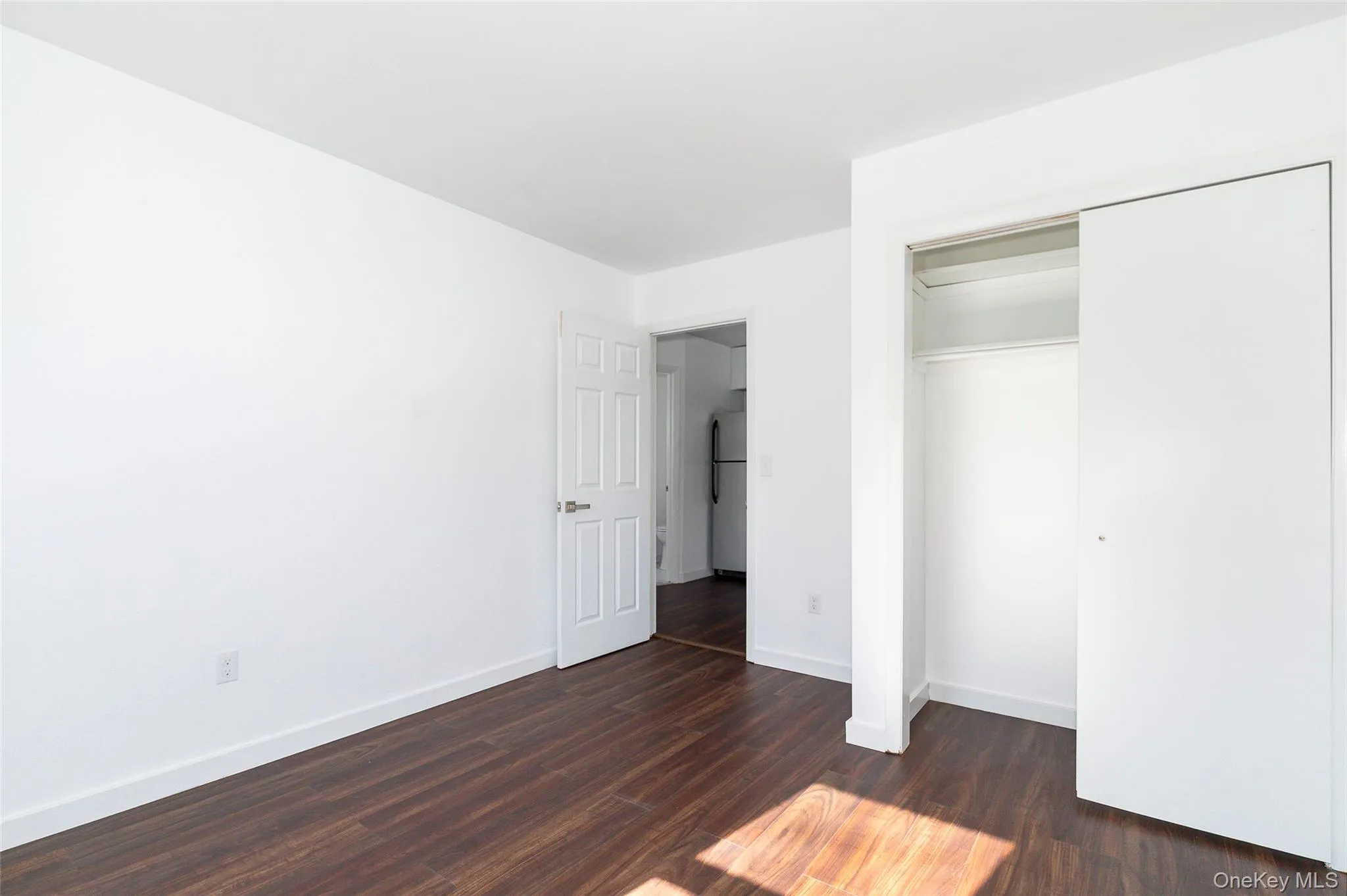 Unfurnished bedroom with white fridge, a closet, and dark hardwood / wood-style floors Unfurnished bedroom with white fridge, a closet, and dark hardwood / wood-style floors