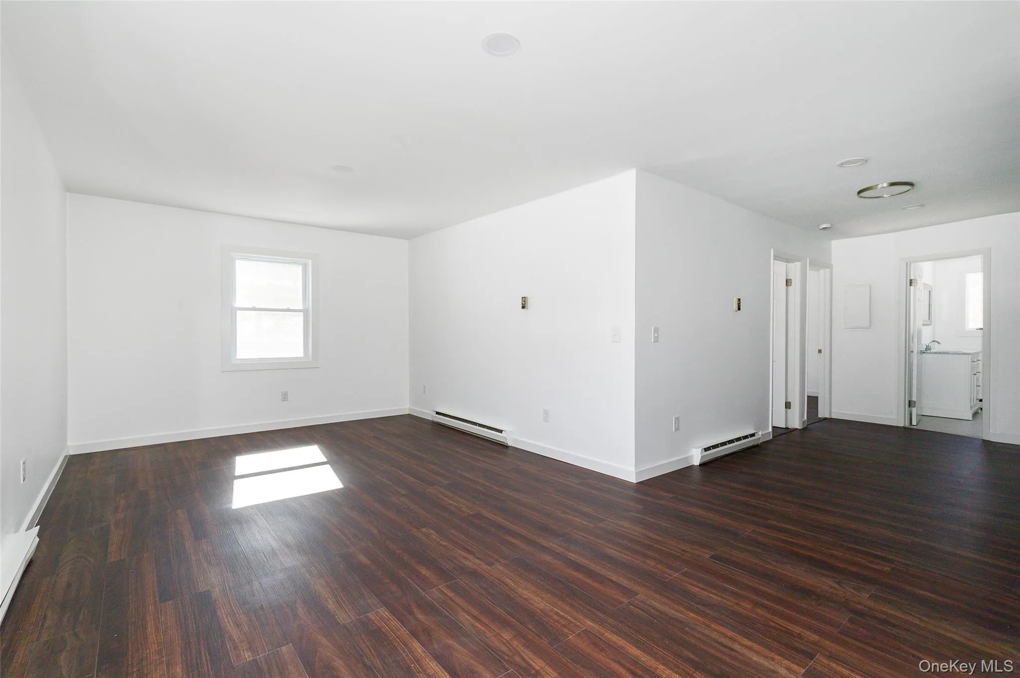 Unfurnished living room with baseboard heating and dark wood-type flooring Unfurnished living room with baseboard heating and dark wood-type flooring