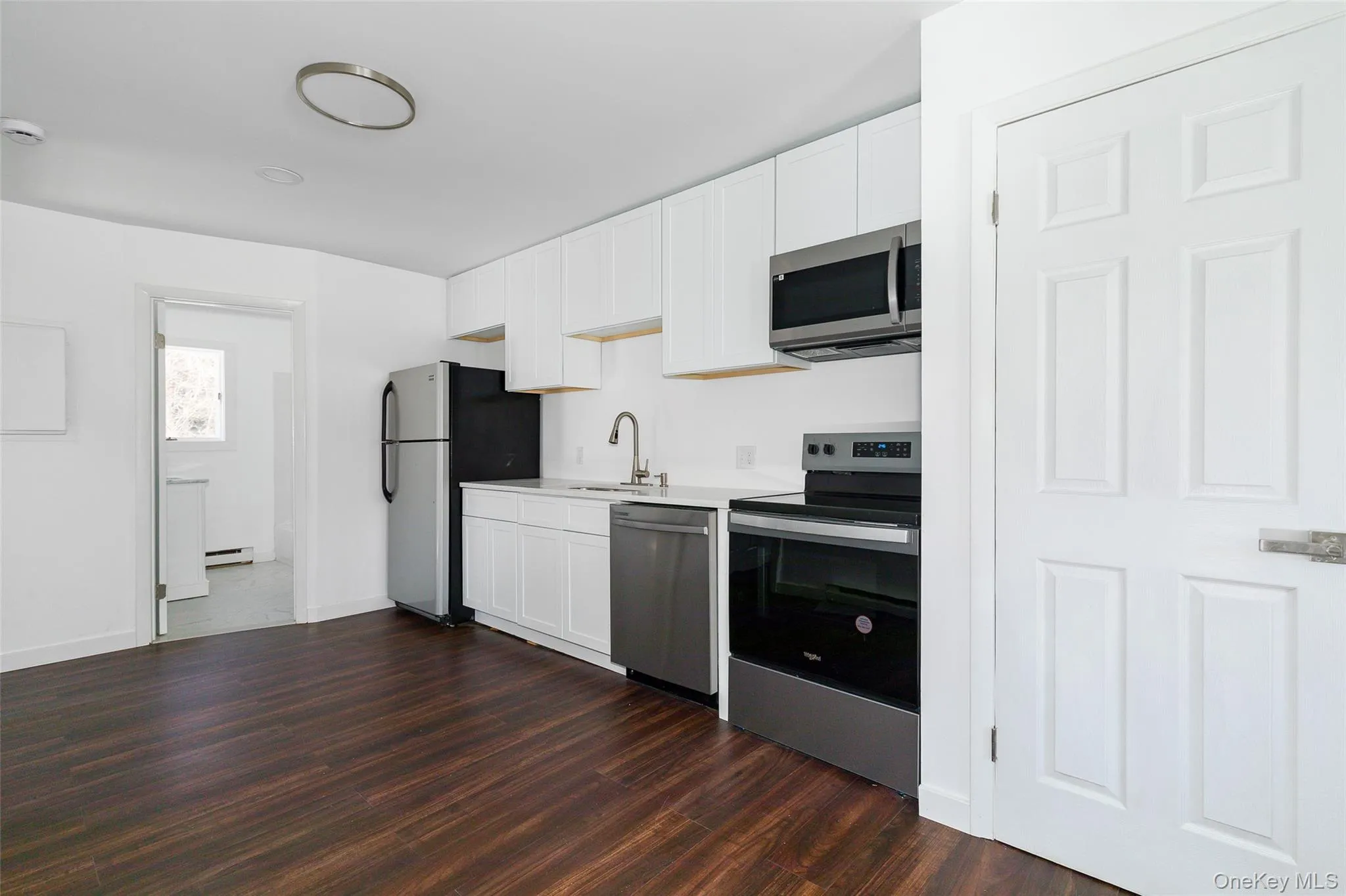 Kitchen featuring baseboard heating, sink, dark wood-type flooring, appliances with stainless steel finishes, quart counters and white cabinets Kitchen featuring baseboard heating, sink, dark wood-type flooring, appliances with stainless steel finishes, quart counters and white cabinets