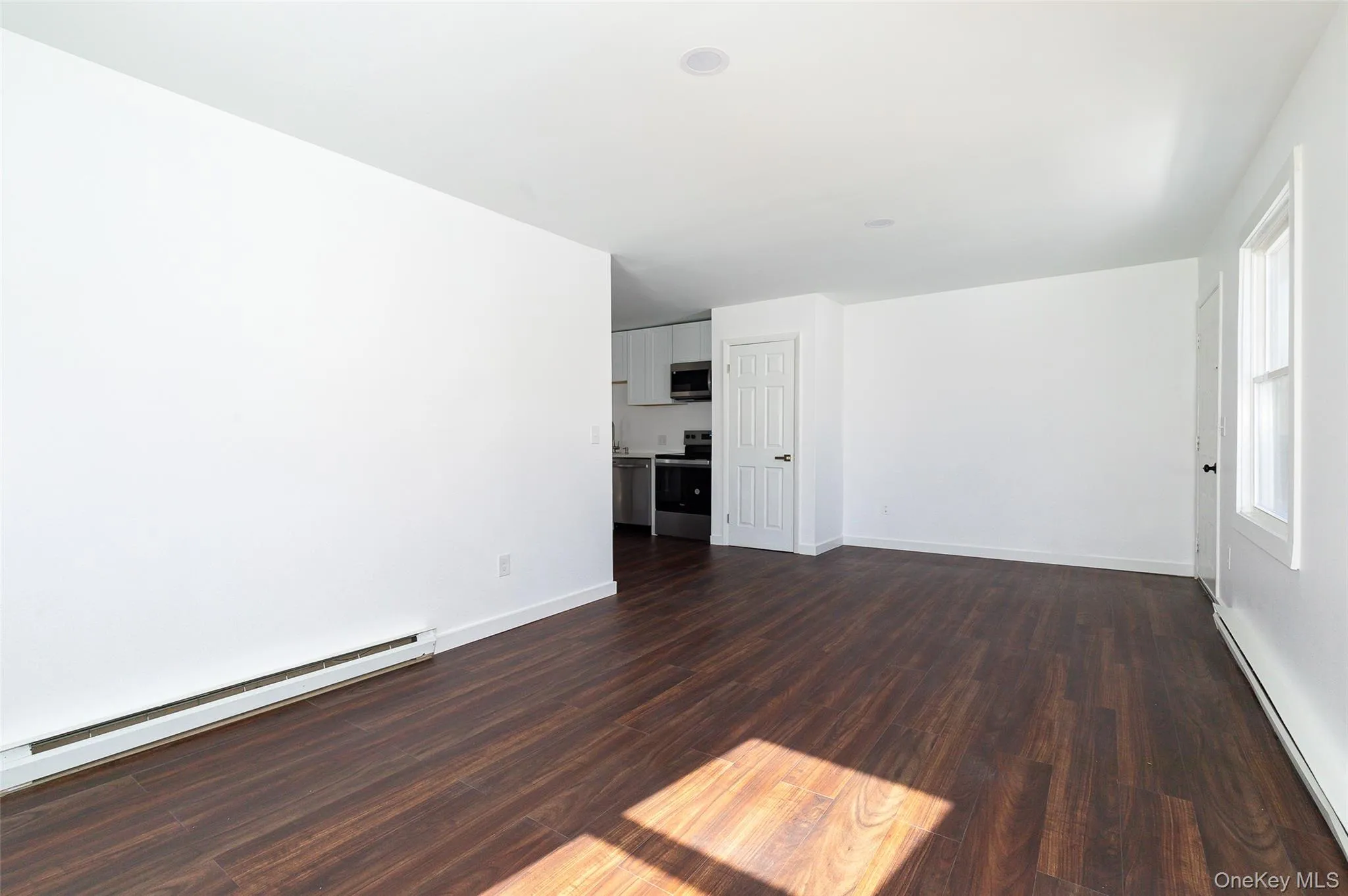 Empty living room featuring dark hardwood / wood-style flooring and a baseboard heating unit Empty living room featuring dark hardwood / wood-style flooring and a baseboard heating unit