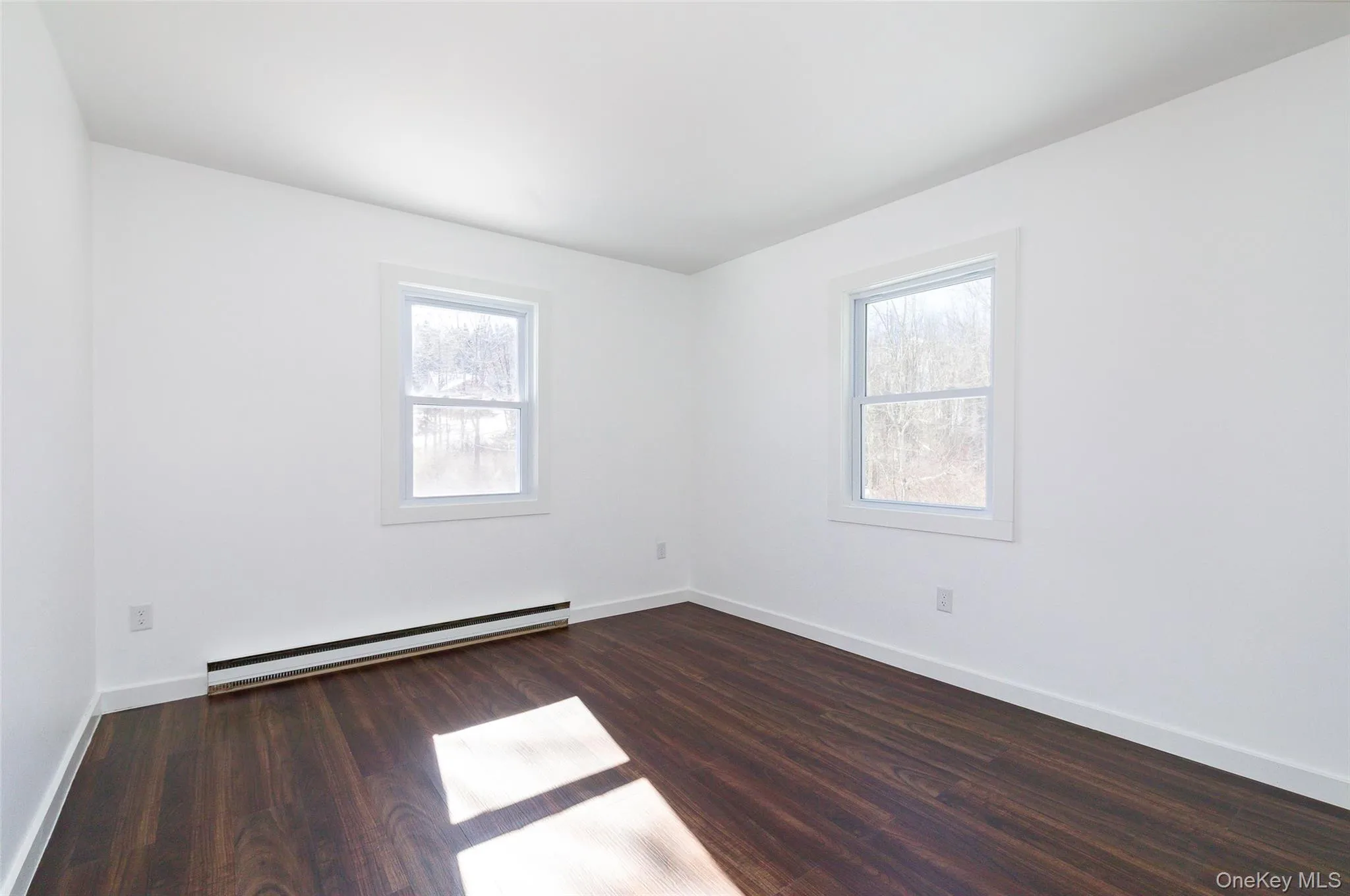 Bedroom with a healthy amount of sunlight, dark wood-type flooring, and a baseboard heating unit Bedroom with a healthy amount of sunlight, dark wood-type flooring, and a baseboard heating unit