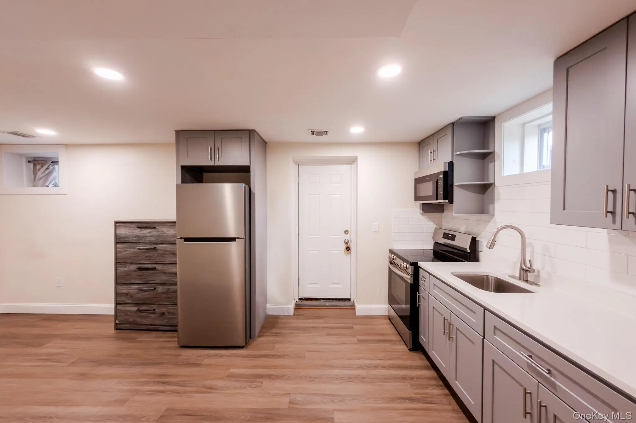 Modern summer kitchen featuring gray shaker cabinetry, stainless steel appliances, a white subway tile backsplash, and light wood-finish flooring Modern summer kitchen featuring gray shaker cabinetry, stainless steel appliances, a white subway tile backsplash, and light wood-finish flooring