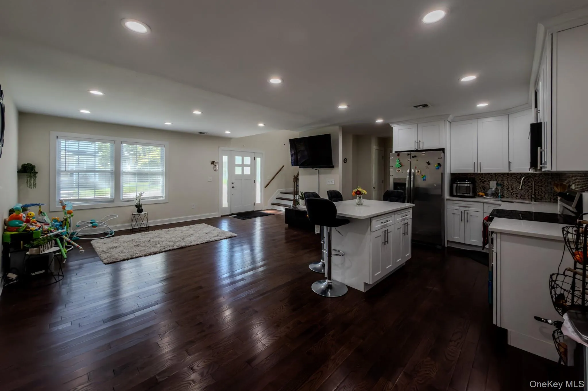Open-concept living space featuring rich wood-finish flooring, recessed lighting, and a white kitchen island with counter seating Open-concept living space featuring rich wood-finish flooring, recessed lighting, and a white kitchen island with counter seating