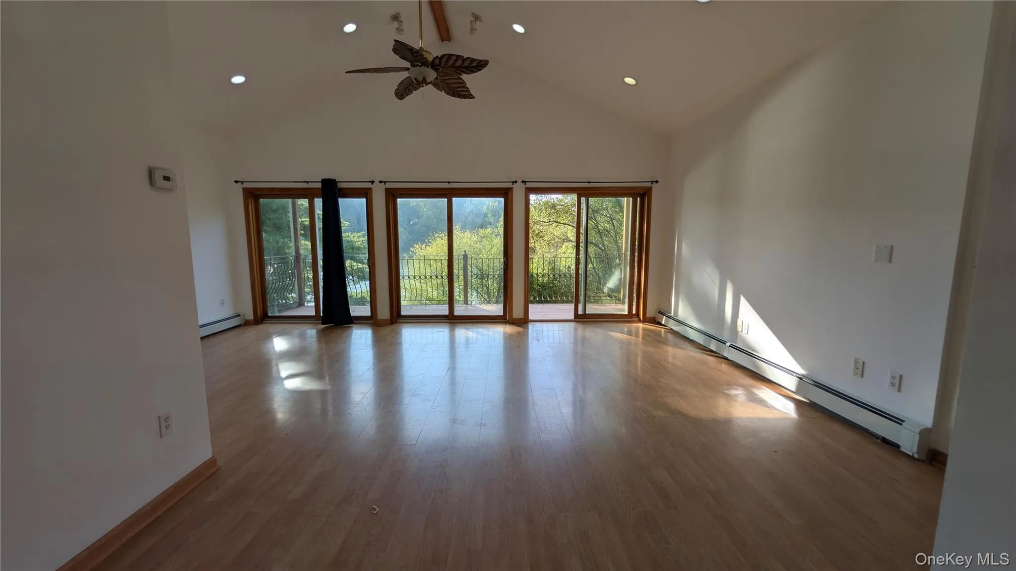 Empty room featuring a baseboard heating unit, high vaulted ceiling, wood finished floors, ceiling fan, and recessed lighting Empty room featuring a baseboard heating unit, high vaulted ceiling, wood finished floors, ceiling fan, and recessed lighting
