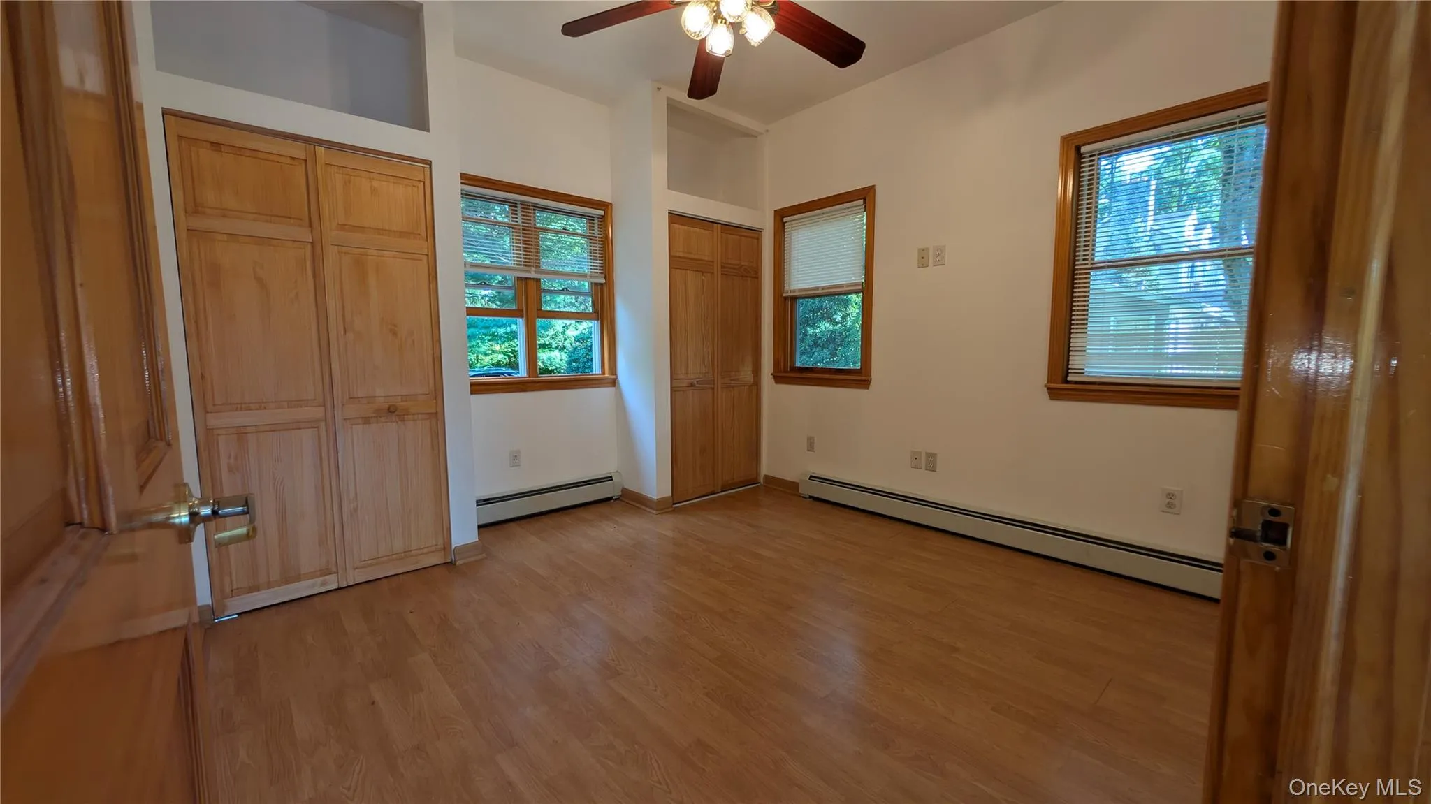 Unfurnished bedroom with two closets, a baseboard radiator, light wood finished floors, and a ceiling fan Unfurnished bedroom with two closets, a baseboard radiator, light wood finished floors, and a ceiling fan