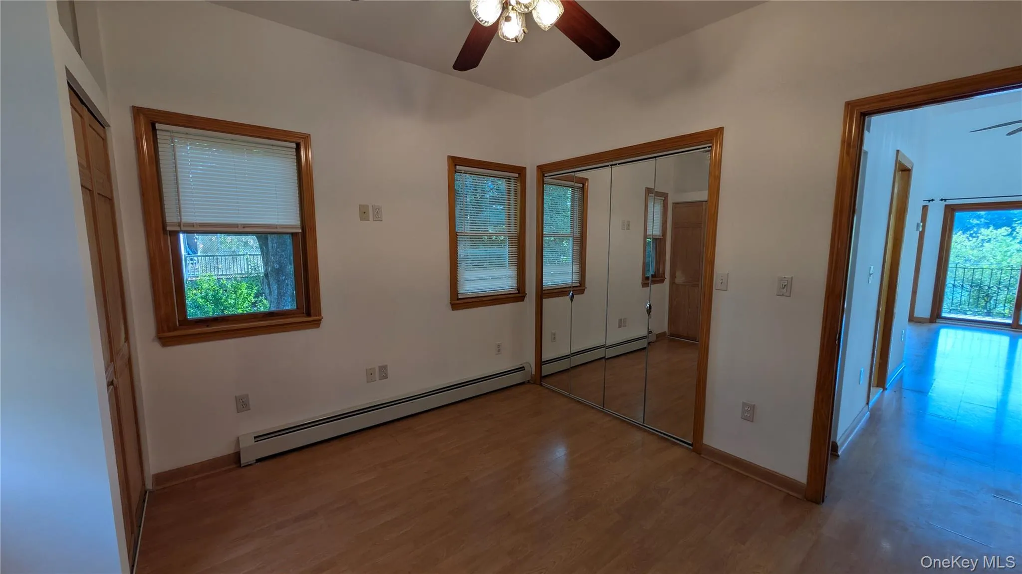 Unfurnished bedroom featuring a closet, wood finished floors, a ceiling fan, and baseboard heating Unfurnished bedroom featuring a closet, wood finished floors, a ceiling fan, and baseboard heating