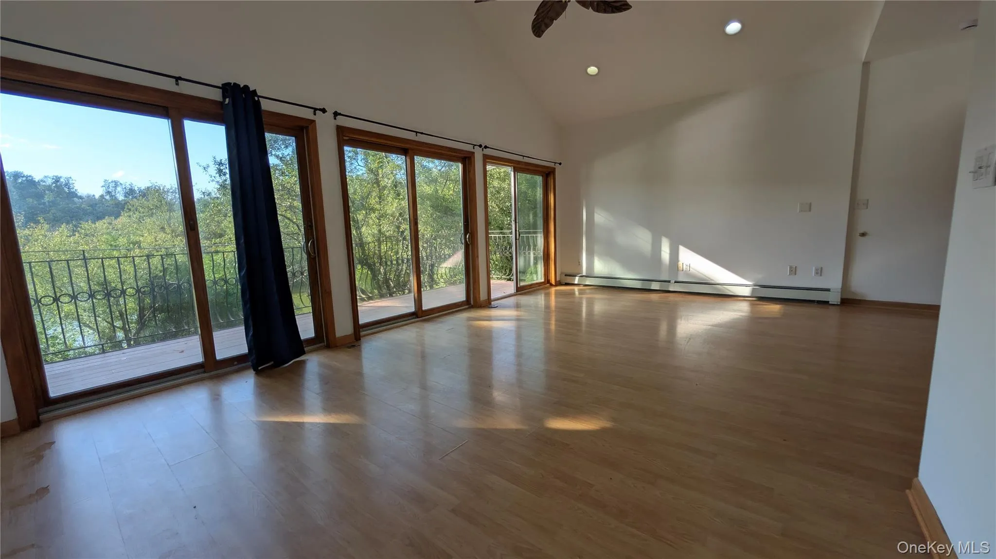 Empty room with high vaulted ceiling, wood finished floors, recessed lighting, a baseboard radiator, and a ceiling fan Empty room with high vaulted ceiling, wood finished floors, recessed lighting, a baseboard radiator, and a ceiling fan