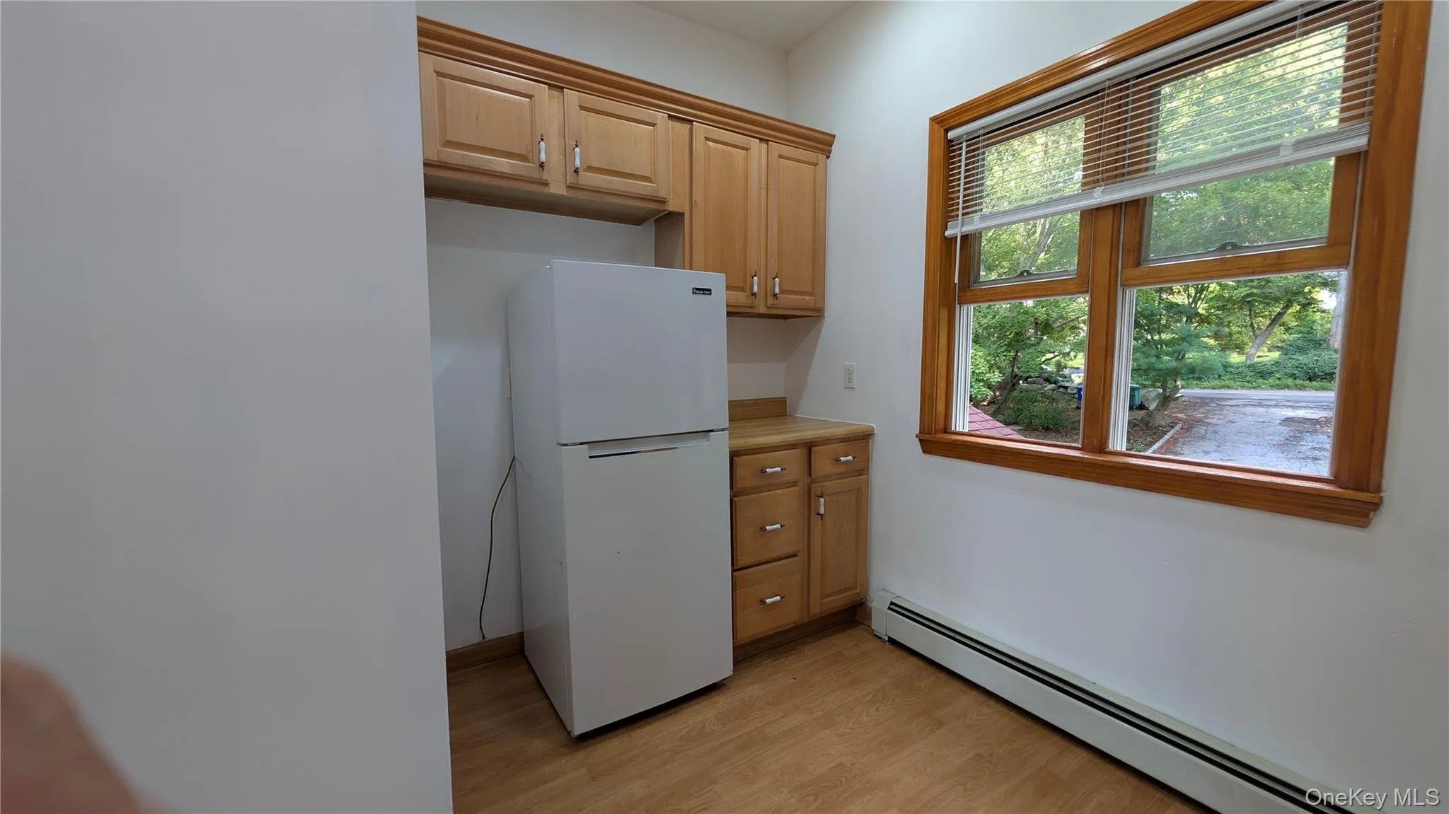 Kitchen with a baseboard radiator, freestanding refrigerator, light wood finished floors, and light countertops Kitchen with a baseboard radiator, freestanding refrigerator, light wood finished floors, and light countertops