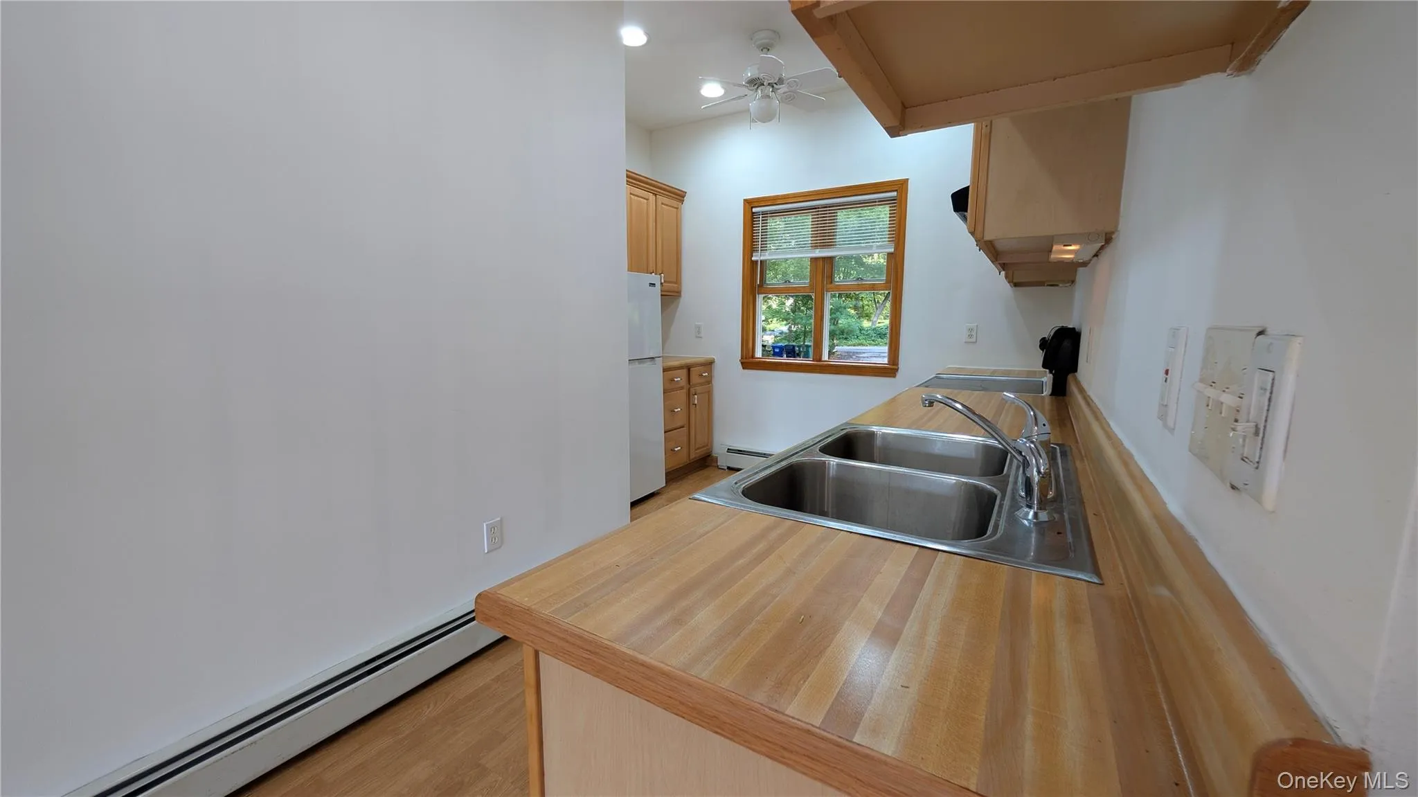 Kitchen with a baseboard radiator, light countertops, light wood-type flooring, freestanding refrigerator, and stove Kitchen with a baseboard radiator, light countertops, light wood-type flooring, freestanding refrigerator, and stove