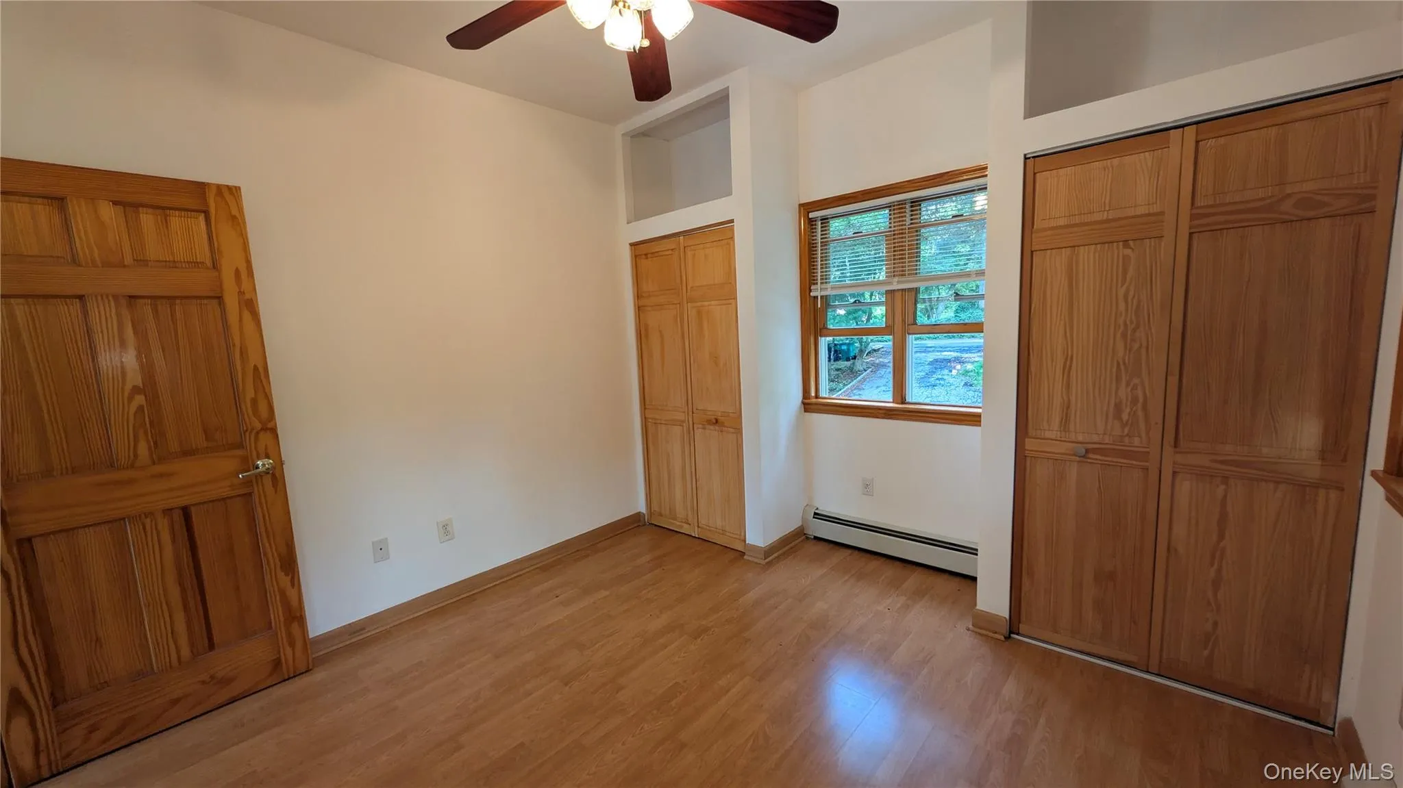 Unfurnished bedroom featuring multiple closets, light wood-style floors, baseboard heating, and ceiling fan Unfurnished bedroom featuring multiple closets, light wood-style floors, baseboard heating, and ceiling fan