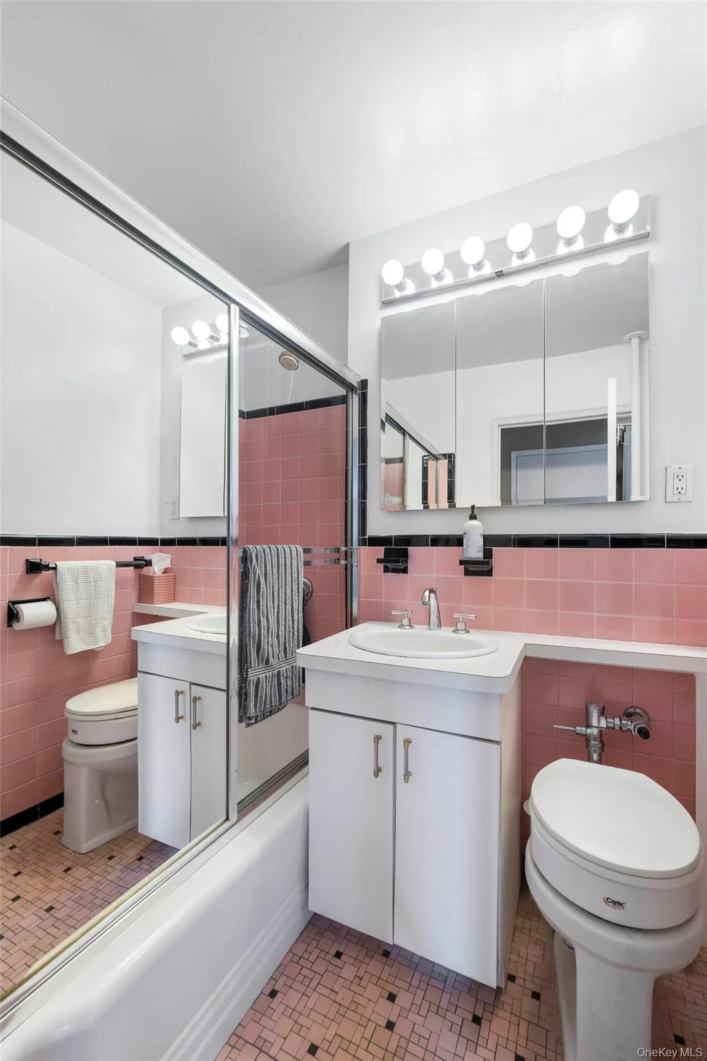 Bathroom featuring a pink and black tiled design, a white vanity with an integrated sink, a mirrored medicine cabinet, a vanity light fixture, and a shower with sliding glass doors Bathroom featuring a pink and black tiled design, a white vanity with an integrated sink, a mirrored medicine cabinet, a vanity light fixture, and a shower with sliding glass doors