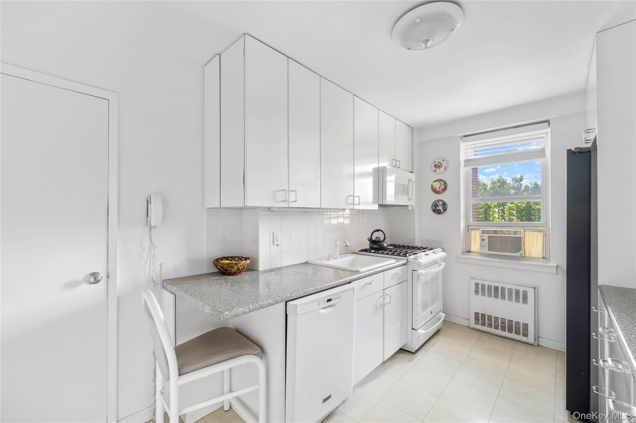 Kitchen featuring white cabinetry with silver hardware, speckled countertops, a white tile backsplash, and linoleum flooring Kitchen featuring white cabinetry with silver hardware, speckled countertops, a white tile backsplash, and linoleum flooring