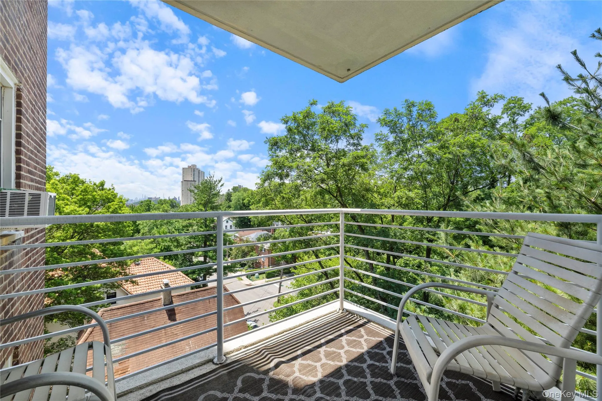 Balcony space featuring a patterned area rug, white metal railing, and a brick exterior wall Balcony space featuring a patterned area rug, white metal railing, and a brick exterior wall
