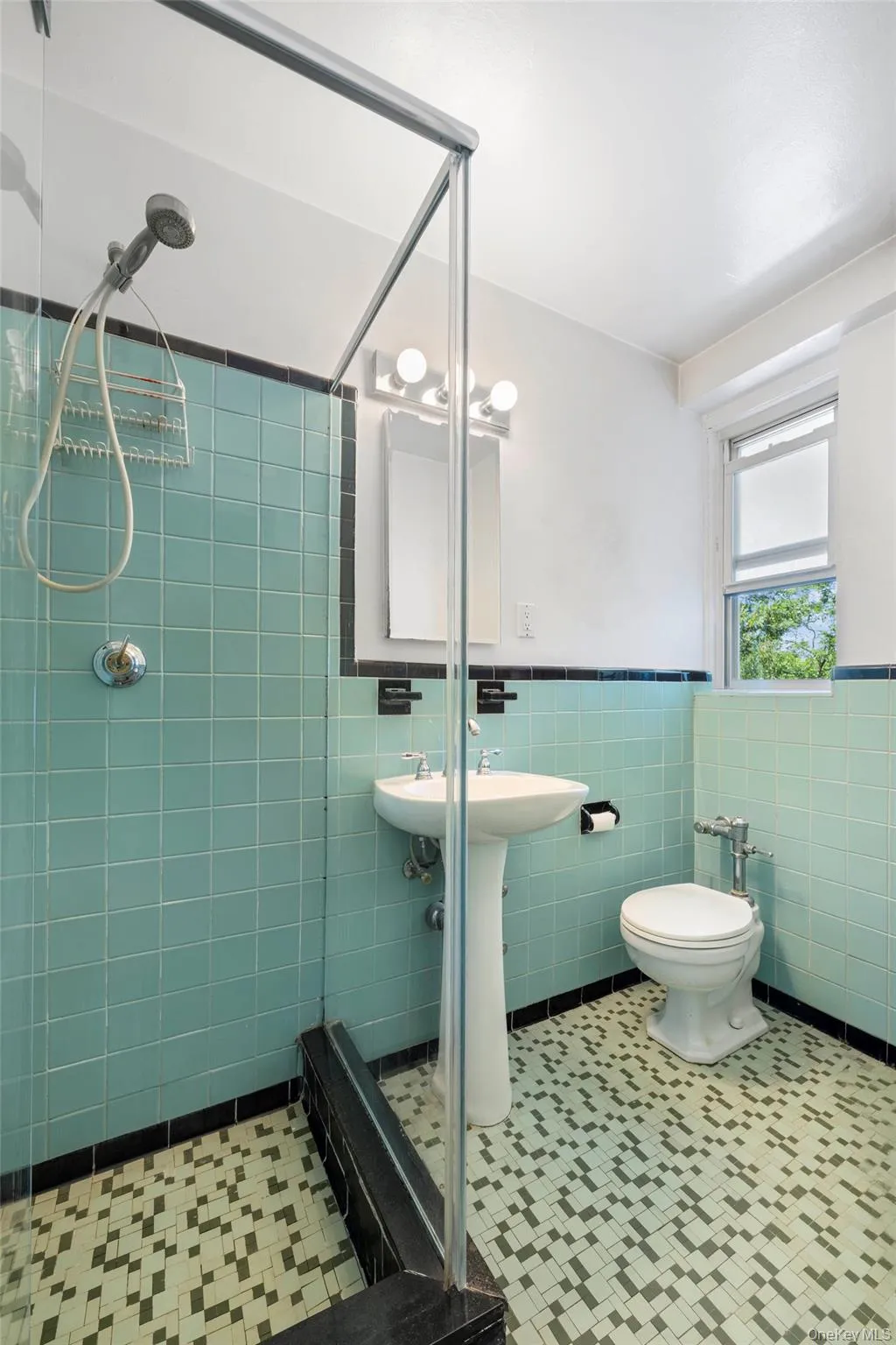 Bathroom featuring a glass-enclosed shower, pedestal sink, and patterned floor tiling Bathroom featuring a glass-enclosed shower, pedestal sink, and patterned floor tiling