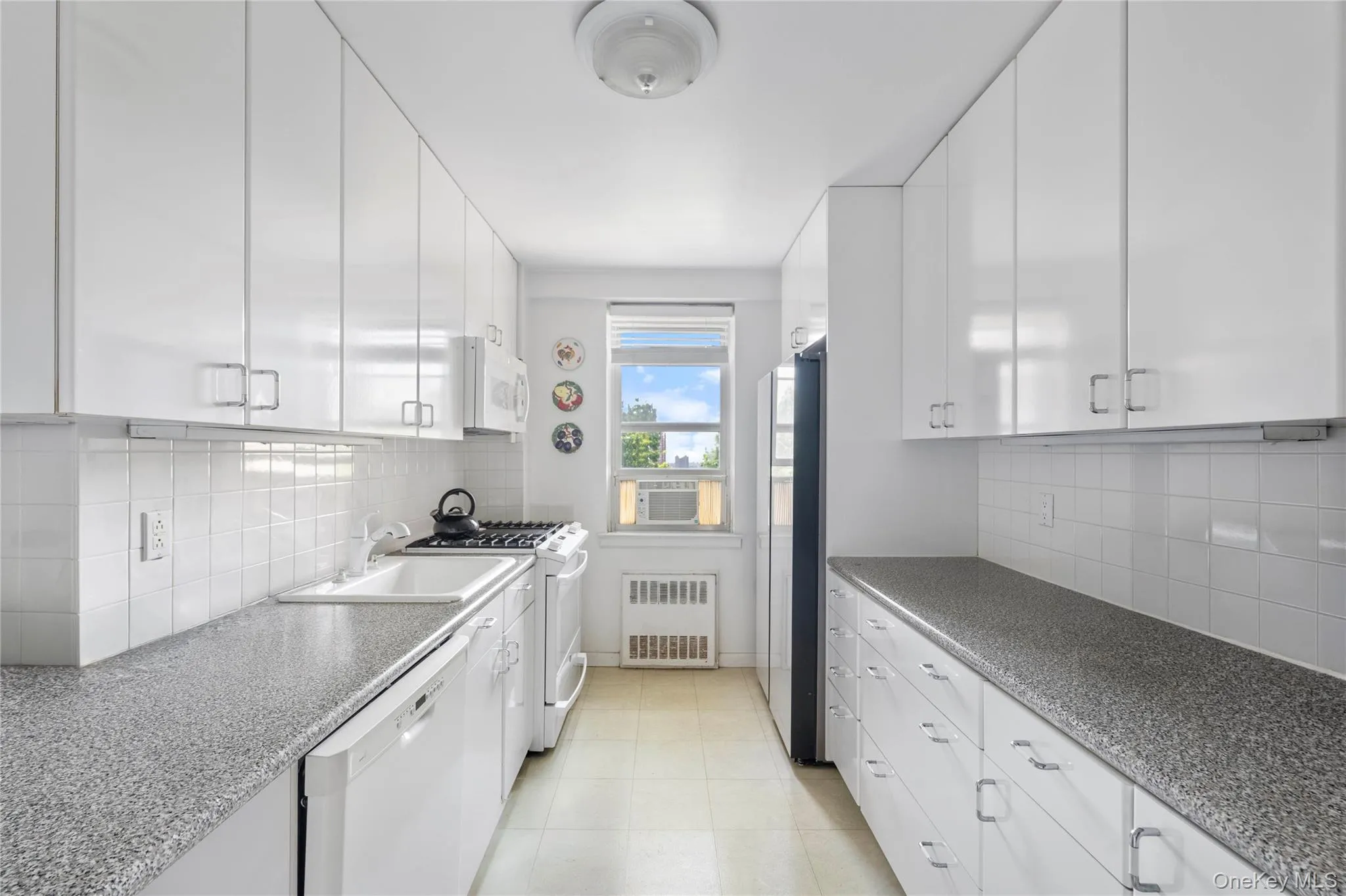 Galley kitchen featuring abundant white cabinetry, a white tile backsplash, and speckled countertops Galley kitchen featuring abundant white cabinetry, a white tile backsplash, and speckled countertops