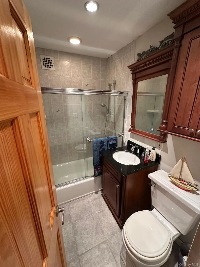 Full bath featuring combined bath / shower with glass door, vanity, and light tile patterned flooring Full bath featuring combined bath / shower with glass door, vanity, and light tile patterned flooring