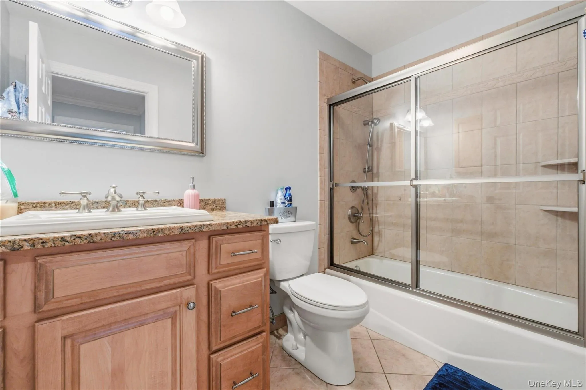 This well-appointed full bathroom includes a warm wood vanity with granite countertop, a large framed mirror, and bright overhead lighting. The tub and shower combination features neutral tile and sliding glass doors, offering both practicality and style. With clean finishes and a cohesive design, this bathroom is move-in ready. This well-appointed full bathroom includes a warm wood vanity with granite countertop, a large framed mirror, and bright overhead lighting. The tub and shower combination features neutral tile and sliding glass doors, offering both practicality and style. With clean finishes and a cohesive design, this bathroom is move-in ready.