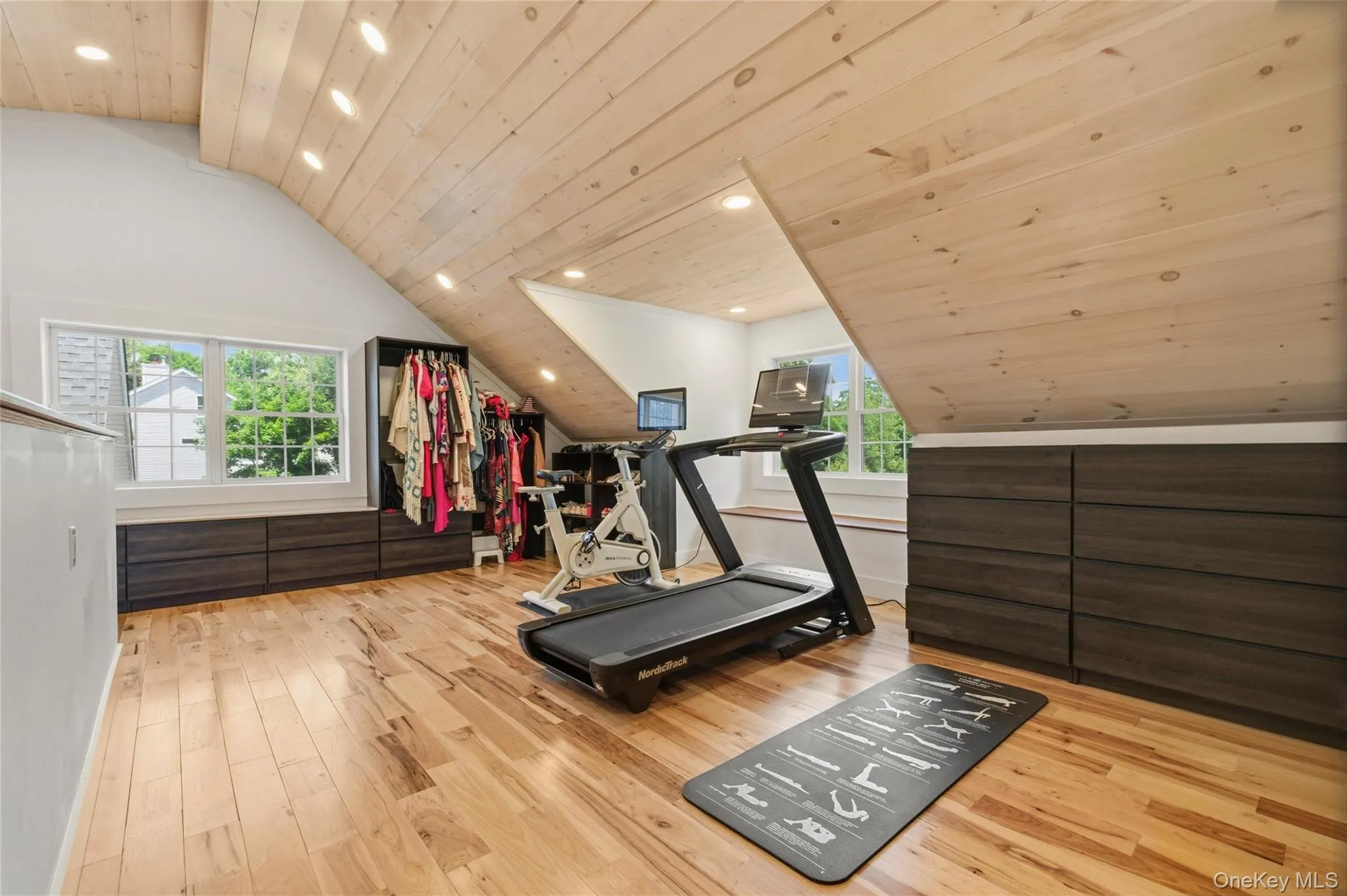 This bright, multi-purpose room combines a home gym with ample closet storage and natural light. The sloped wood ceiling and built-ins create a warm, functional space for fitness and organization. This bright, multi-purpose room combines a home gym with ample closet storage and natural light. The sloped wood ceiling and built-ins create a warm, functional space for fitness and organization.