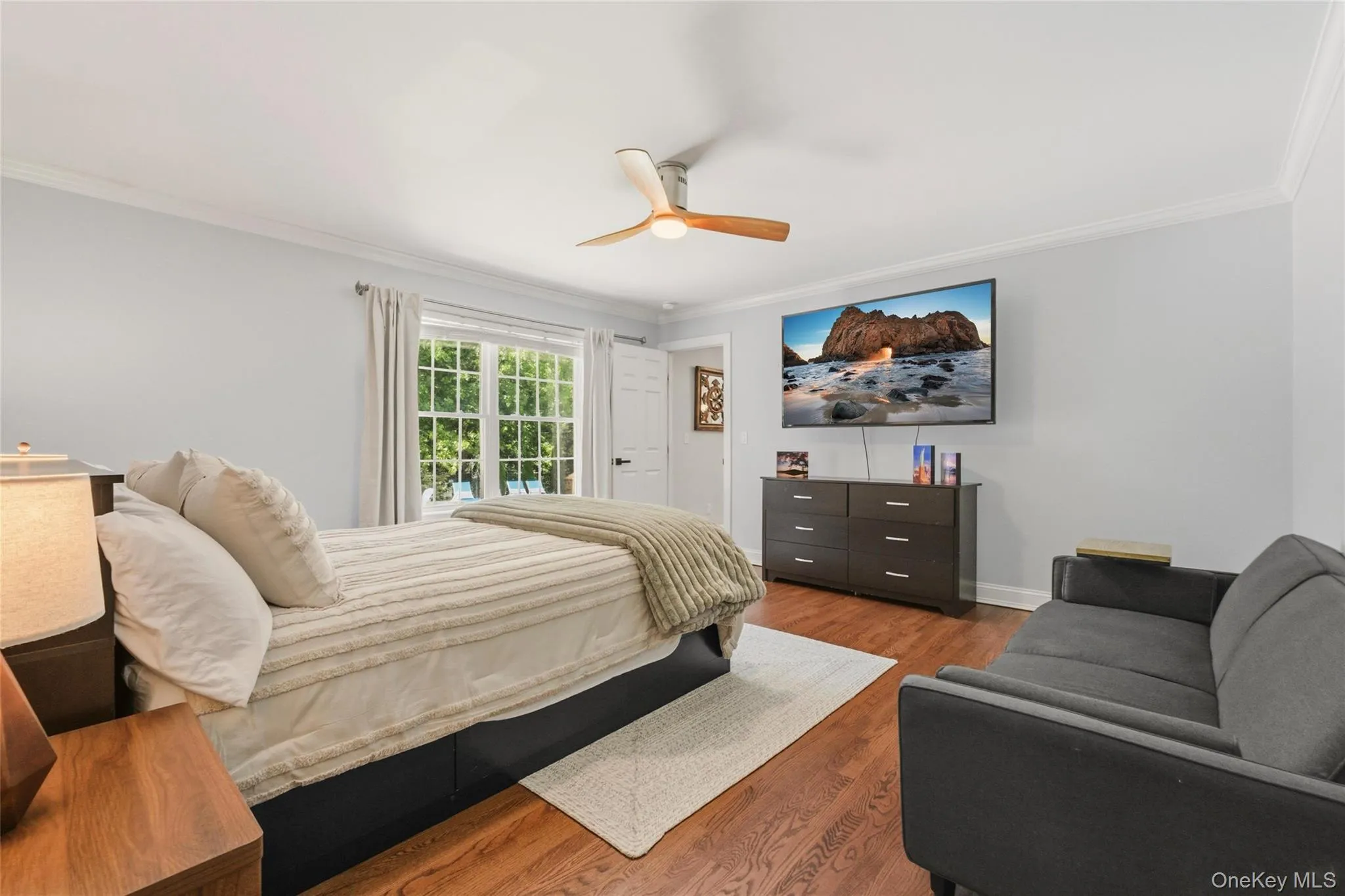 The first of 2 primary suites in the home. This bright and inviting bedroom features a large window, warm hardwood floors, and a cozy seating area for added comfort. A relaxing retreat with modern touches. The first of 2 primary suites in the home. This bright and inviting bedroom features a large window, warm hardwood floors, and a cozy seating area for added comfort. A relaxing retreat with modern touches.