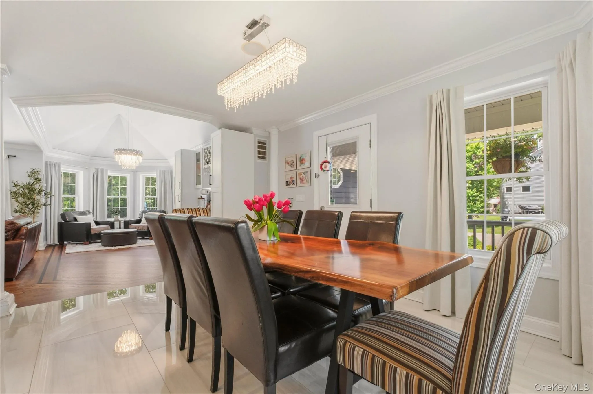 A striking crystal chandelier that elevates the room’s ambiance. Large windows with soft white curtains illuminate the space, while the open layout flows seamlessly into a cozy sitting area with additional seating and warm wood flooring. The combination of modern finishes and classic touches makes this an ideal setting for family meals and entertaining. A striking crystal chandelier that elevates the room’s ambiance. Large windows with soft white curtains illuminate the space, while the open layout flows seamlessly into a cozy sitting area with additional seating and warm wood flooring. The combination of modern finishes and classic touches makes this an ideal setting for family meals and entertaining.