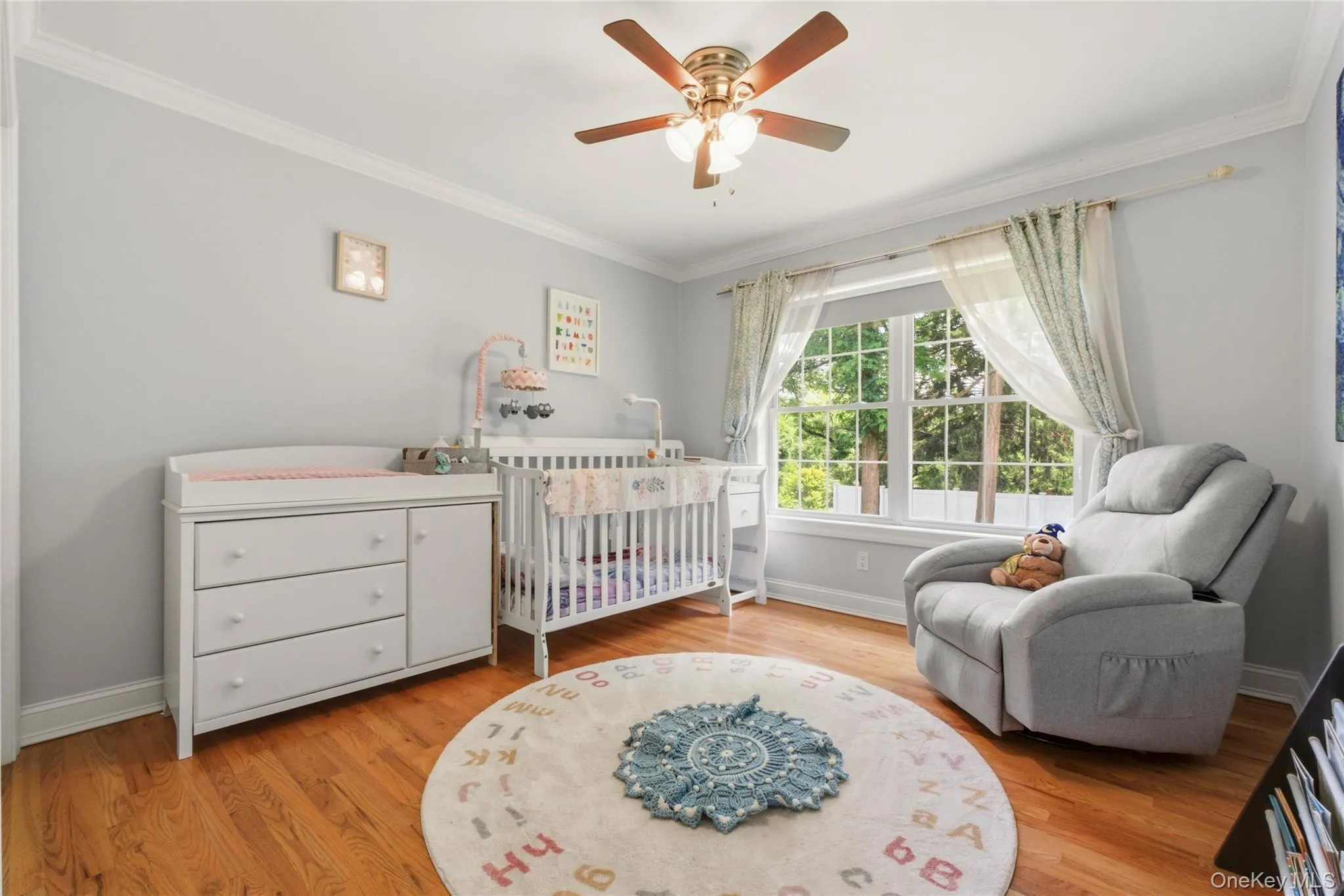 This charming nursery is designed with comfort and care in mind, featuring soft gray walls, warm wood flooring, and a large window that fills the room with natural light. This charming nursery is designed with comfort and care in mind, featuring soft gray walls, warm wood flooring, and a large window that fills the room with natural light.