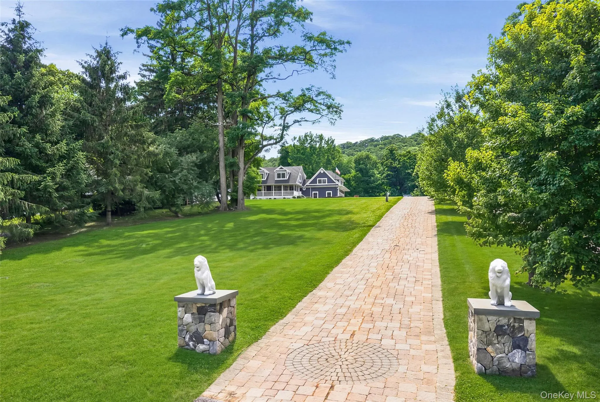 Paved driveway featuring a circular paver design, flanked by manicured lawns and mature trees Paved driveway featuring a circular paver design, flanked by manicured lawns and mature trees