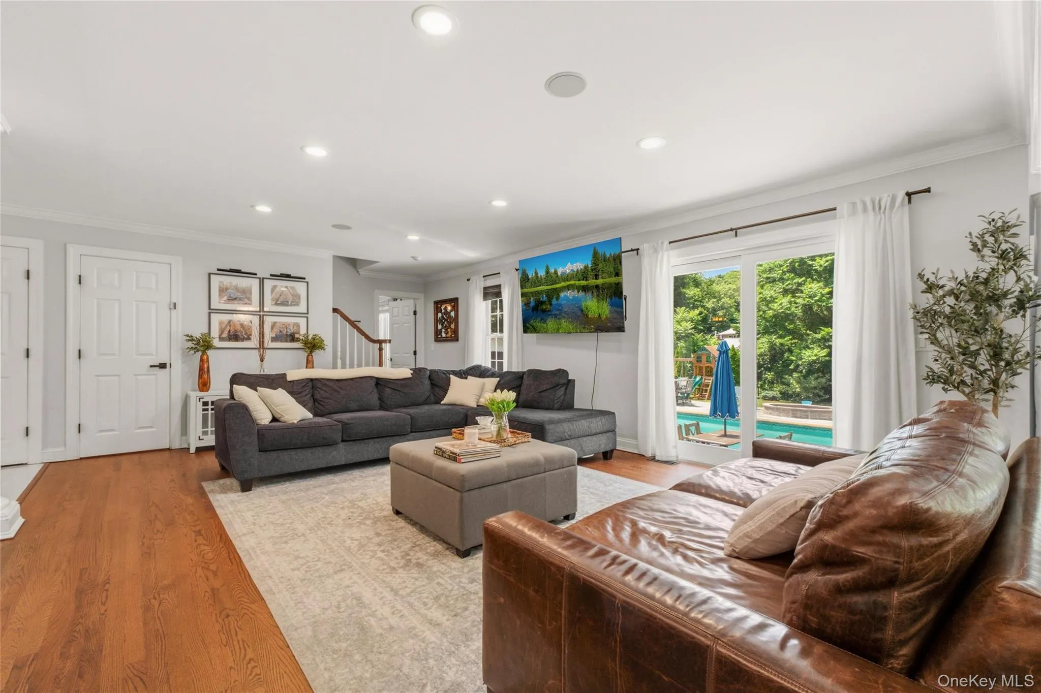 Large glass doors flood the room with natural light and open directly to the backyard oasis, complete with a pool, patio seating, and lush greenery. Warm wood floors, and a mounted TV create a relaxed yet refined atmosphere ideal for everyday living and entertaining. Large glass doors flood the room with natural light and open directly to the backyard oasis, complete with a pool, patio seating, and lush greenery. Warm wood floors, and a mounted TV create a relaxed yet refined atmosphere ideal for everyday living and entertaining.