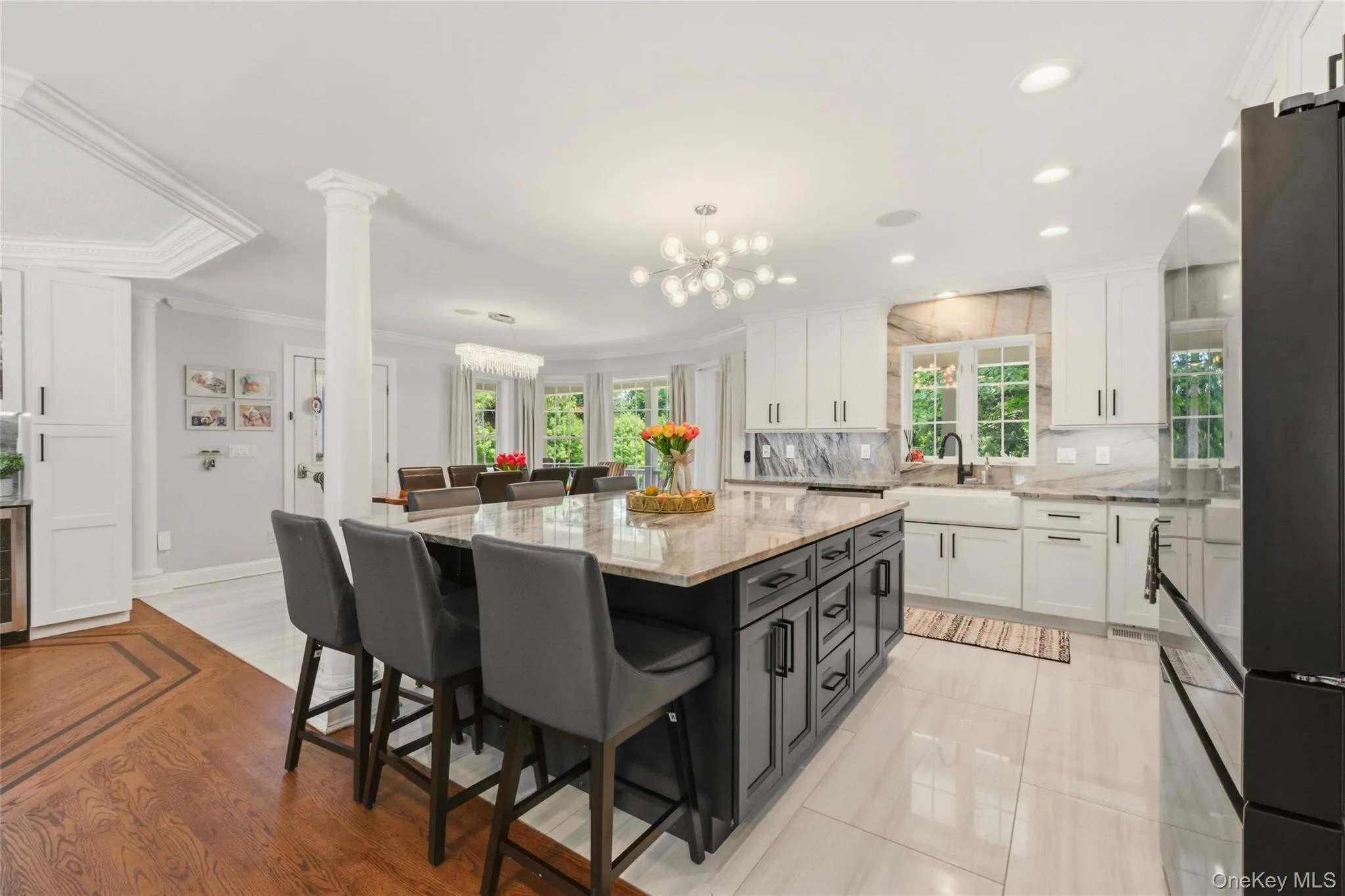 This bright and spacious open-concept kitchen and dining area blends style and functionality. The kitchen boasts a large quartzite-topped island, white cabinetry, and a farmhouse-style sink framed by oversized windows. With seamless transitions between tile and hardwood flooring, this space is ideal for hosting family meals and gatherings. This bright and spacious open-concept kitchen and dining area blends style and functionality. The kitchen boasts a large quartzite-topped island, white cabinetry, and a farmhouse-style sink framed by oversized windows. With seamless transitions between tile and hardwood flooring, this space is ideal for hosting family meals and gatherings.